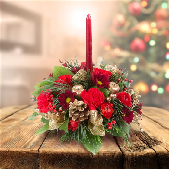 Merry Magic Centerpiece  - Bring the enchantment of the season to your table with our Merry Magic Centerpiece. This festive design sparkles with classic Christmas charm, featuring lush evergreens arranged around vibrant red blooms, crisp white accents, and shimmering holiday ornaments. A glowing candle rises at the center, casting a warm, cozy light that makes every gathering feel extra special. Perfect for holiday dinners, gift-giving, or adding a touch of Christmas wonder to any space, this centerpiece captures the true joy and magic of the season.