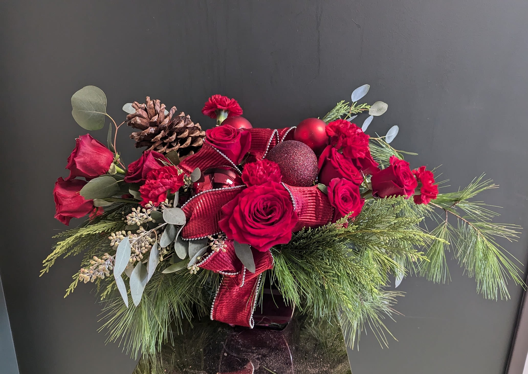 Red Holiday Centerpiece Deluxe - All red is such a luxurious look for the holidays. This arrangement captures is filled with the good stuff, Ecuadorian roses, red carnations for longevity, mini carnations, several types of Christmas greens, trim and  the elegance and grace of the season. 
