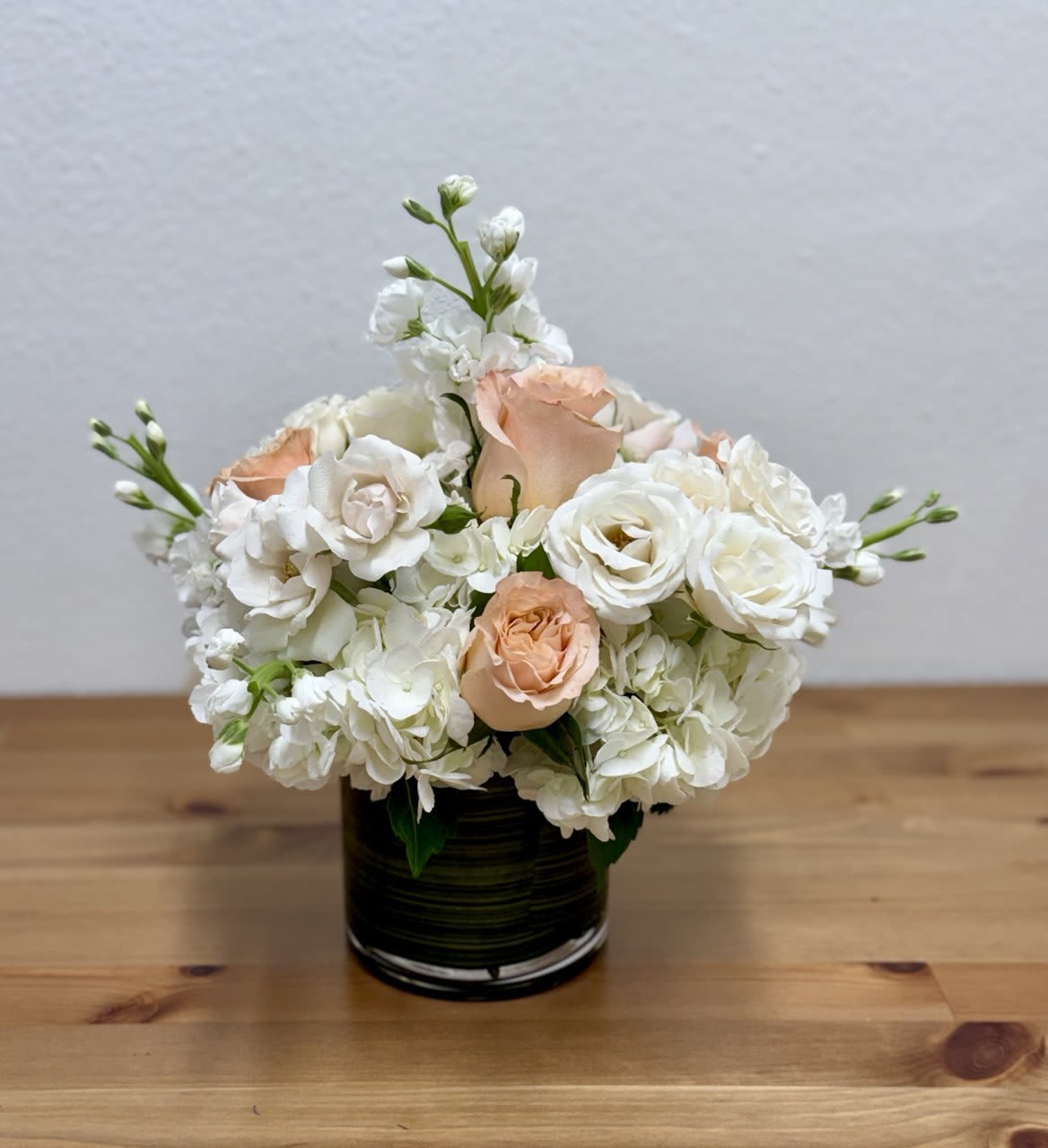Shimmer - Gorgeous flower arrangement made in a cylinder vase, a fabulous way to celebrate any occasion This beautiful vase is arranged with white hydrangea, white stocks, light peach shimmer roses, and white spray roses.