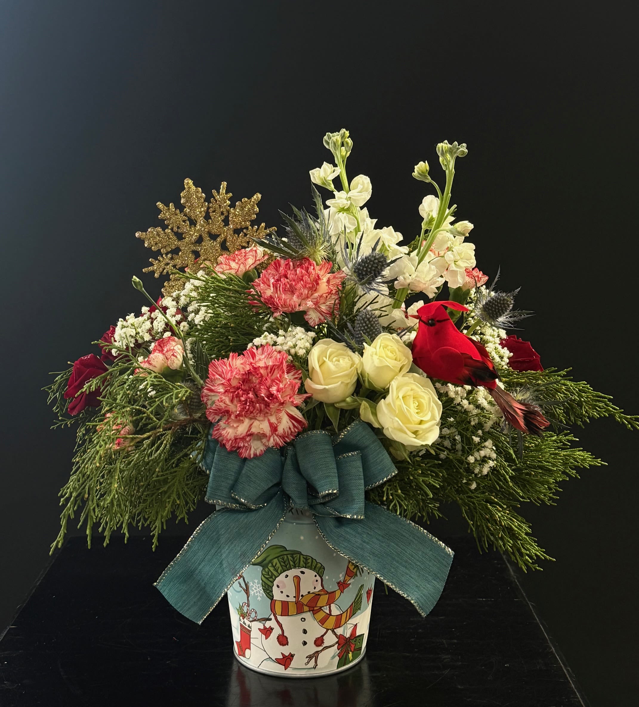 Snowy Snowman - A wintery and adorable arrangement with a little snowflake and cardinal, .spray roses, carnations, mini carnations, stock, thistle, baby's breath and juniper. Container varies