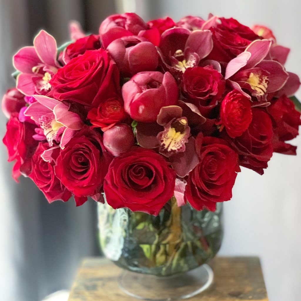 Ruby - Gorgeous red roses, orchids and ranunculus in pretty smokey black pedestal vase. Perfect gift to say I love you. Luxurious and elegant for Valentines Day. Same day delivery available from the best florist in new york city.