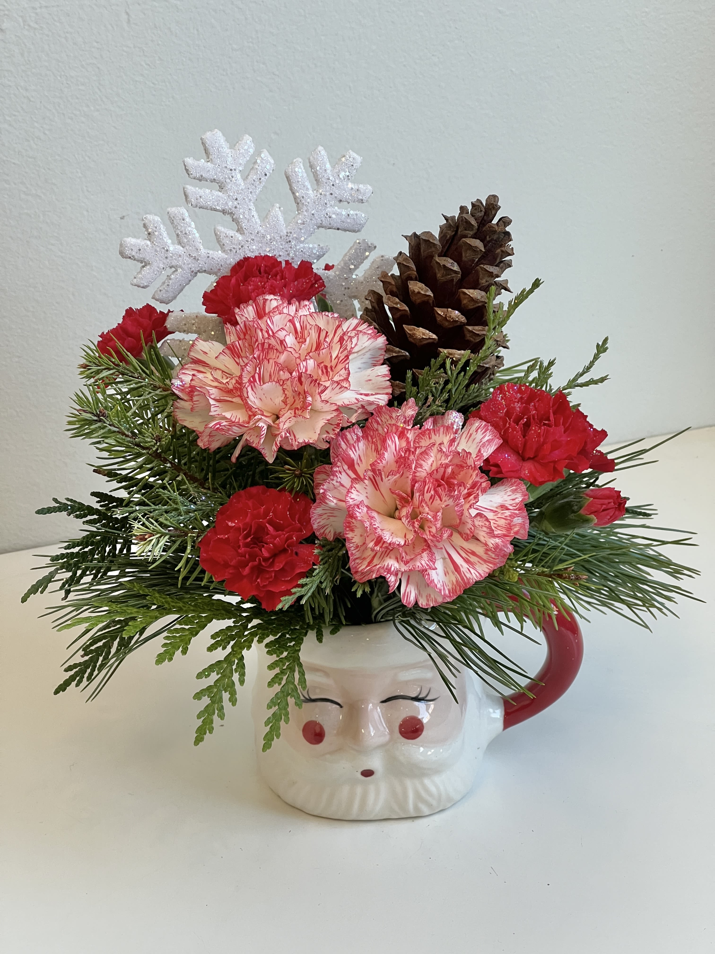 HOL-25-14 - Red/White Carnations, Pixie Carnations, Assorted Winter Greens in a Santa Mug Accented with a Snowflake.