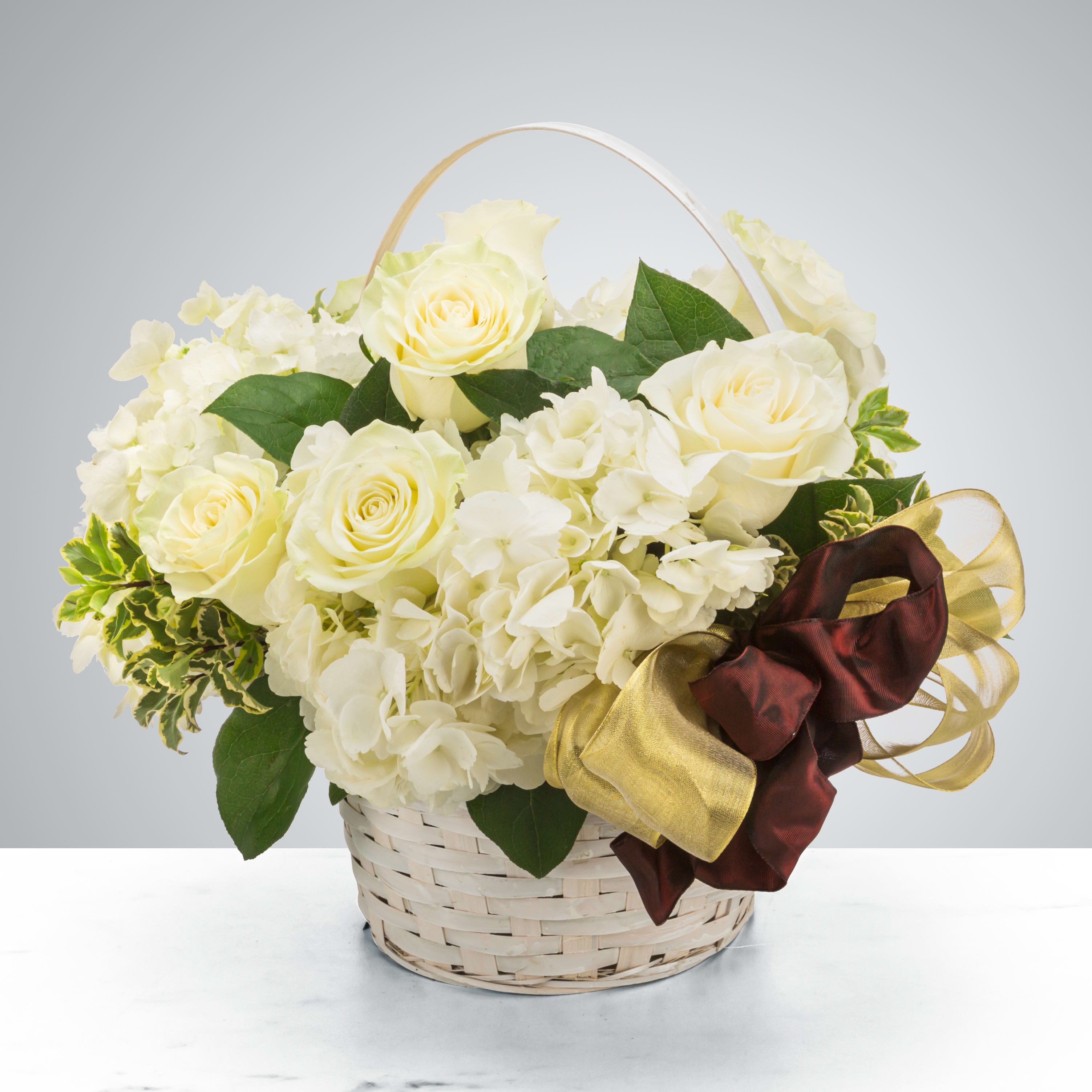 Snowglobe - White fluffy roses and hydrangeas sit in an all-white basket with a gold and maroon ribbon. Send this to celebrate the winter season! Perfect for all the winter holidays like New Year, Hanukkah, Kwanzaa, and Christmas.  Approximate Dimensions: 14"D x 14"H