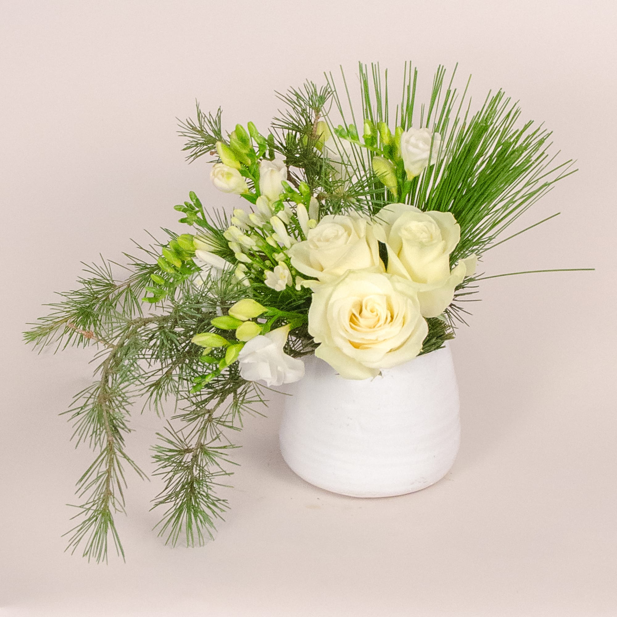Winter wonderland - A clean and elegant look of low compact arrangement for this Holidays Season. Comprised of white Tibet roses, freesias, silver king, needle pine and tree branches.  Size: 14"w x 10"d x 10"h as shown