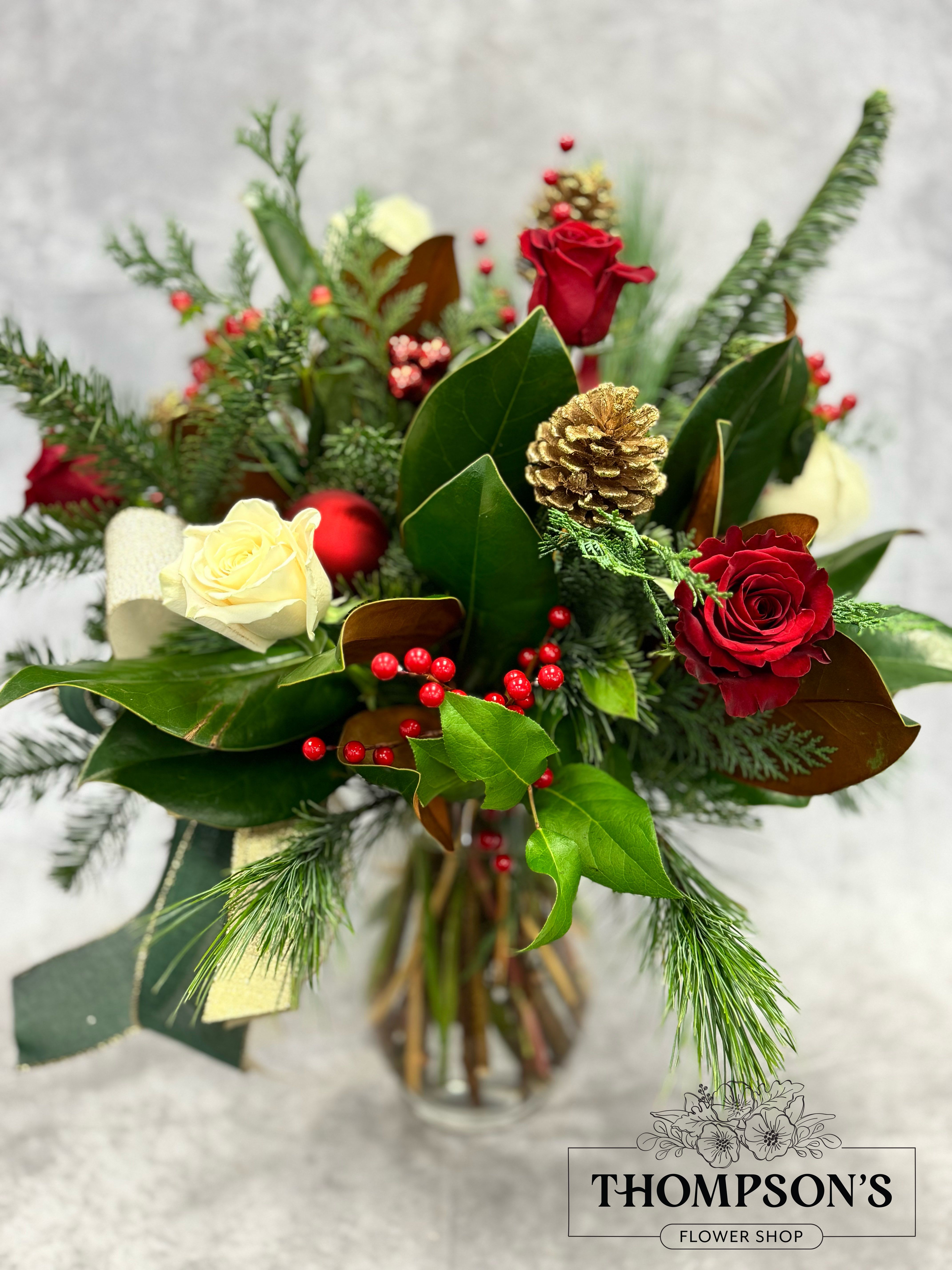Evergreen - Bring home the timeless beauty of the season with Evergreen, a stately holiday vase arrangement standing approximately two feet tall. Rich red roses and creamy white roses are nestled among winter greens, magnolia foliage, bright berry clusters, and shimmering gold pinecones. Finished with festive ribbon and red ornament accents, this design blends classic Christmas color with natural winter charm. Perfect for holiday tables, foyers, kitchen islands, or gifting when you want something impressive and full of seasonal warmth.