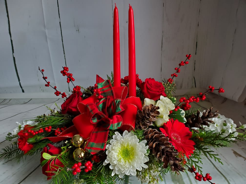 All is Bright - Bring holiday cheer to your table with this festive centerpiece featuring bright white mums, joyful Gerbera daisies, red roses, and winter berries nestled in lush seasonal greens. Accented with pinecones and traditional holiday ribbon, it’s finished with two red taper candles for a warm, glowing touch.