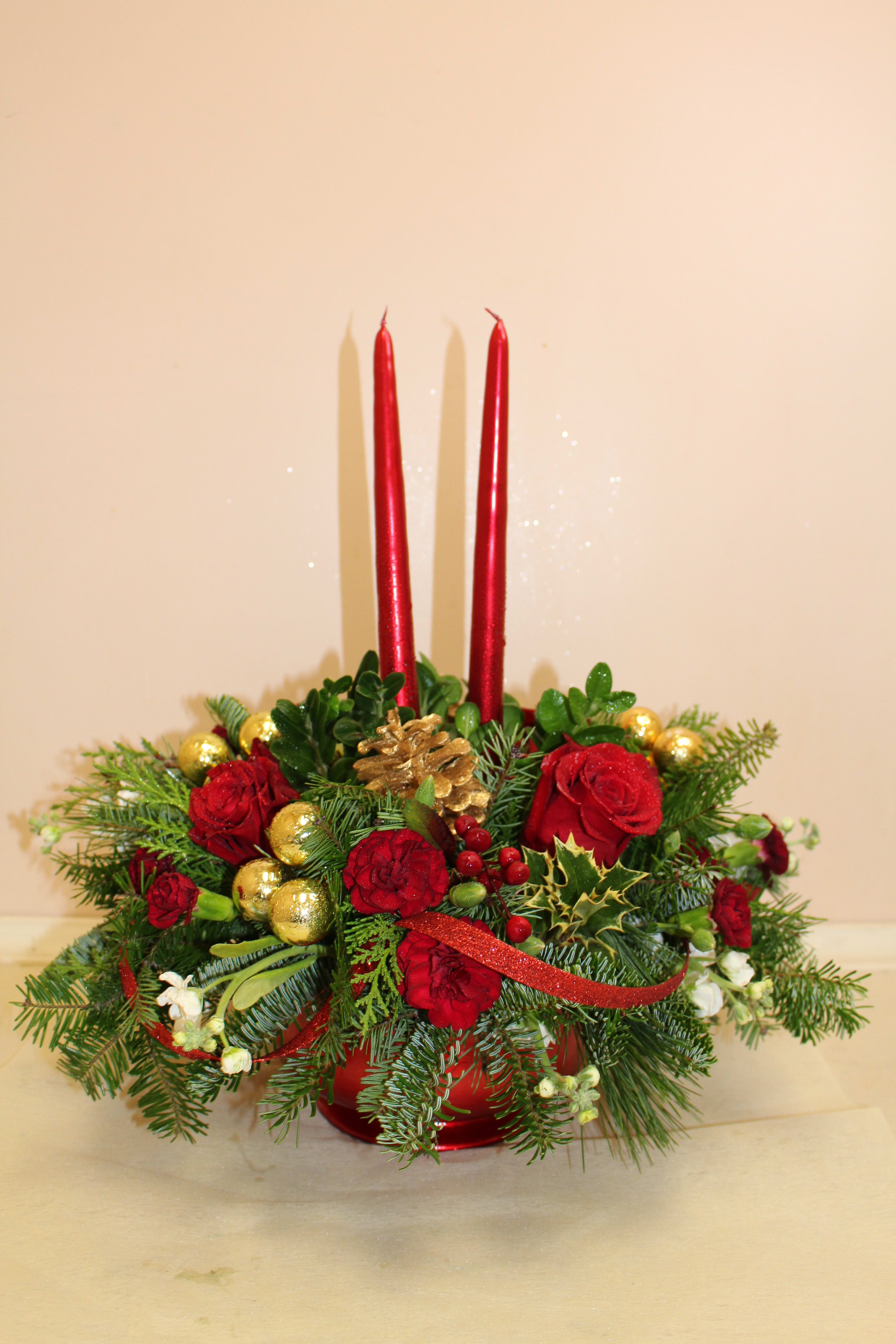 Crimson Rose Centerpiece - This floral Christmas centerpiece will be the star of the table! Take your holiday celebrations to the next level with glowing tapers above crimson red roses ceramic keepsake vase. Sending flowers for Christmas as sure to make spirits bright. Red roses, red carnations and miniature red carnations are arranged with an assortment of holiday greens. 