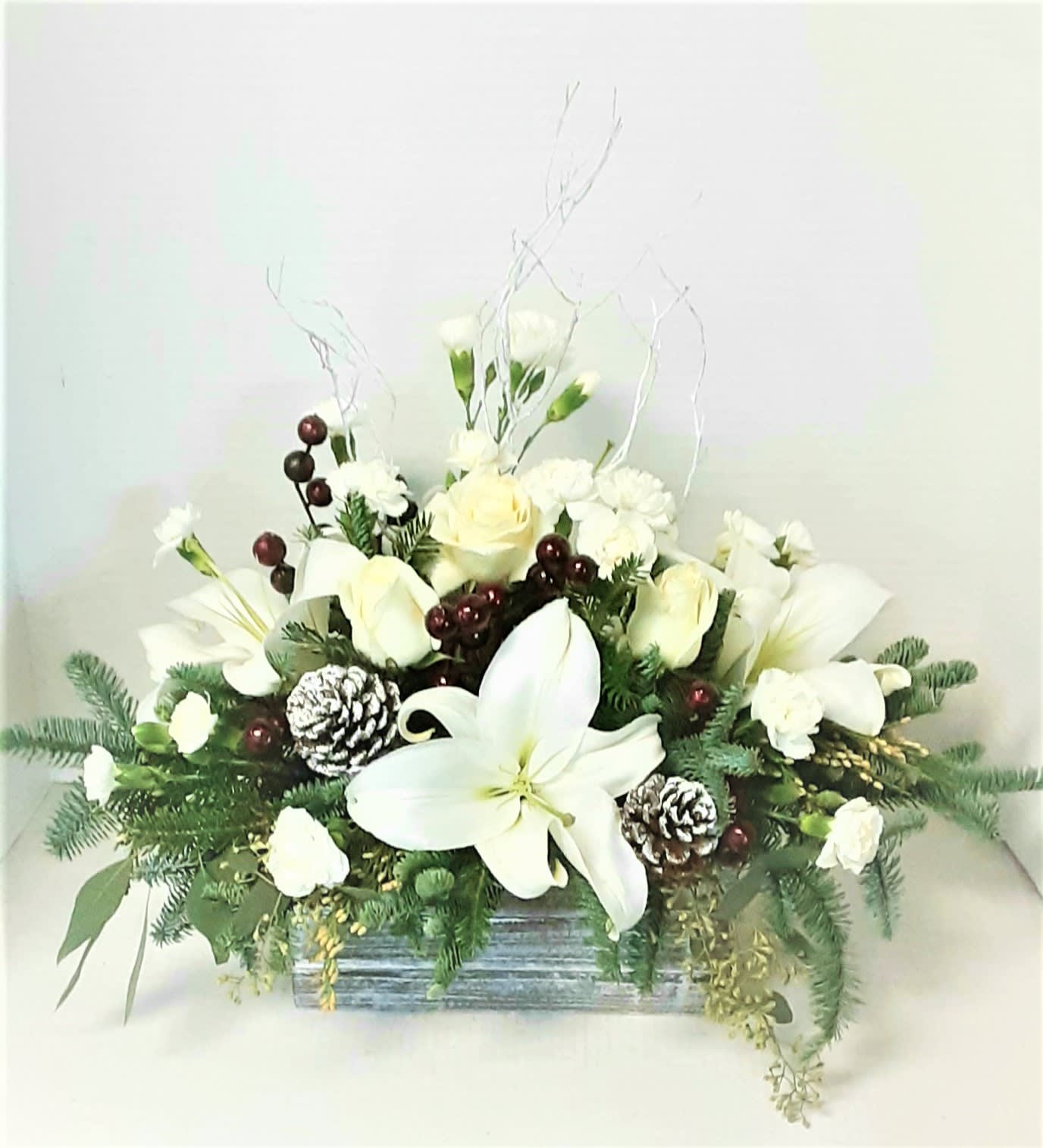 Woodland Box of Winter - All white flowers, roses, lilies, and miniature carnations, with  snowy pine cones and branches surrounded by fragrant Christmas greenery and berries in a rectangular wooden box ..Some flowers may vary.