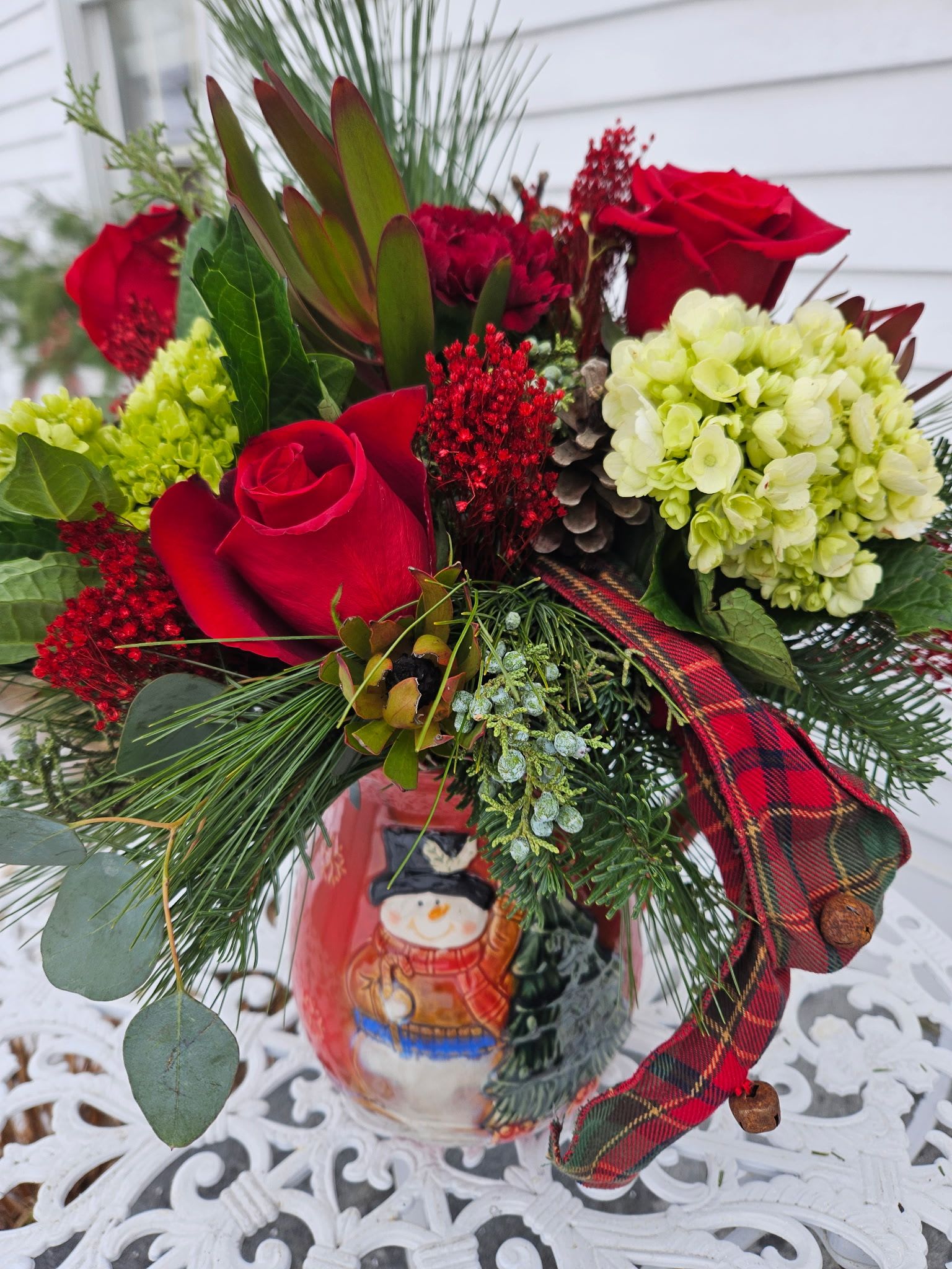 Christmas Country Pitcher - Green hydrangea, red roses, burgundy chrysanthemums, with Christmas greenery in a glazed ceramic pitcher.