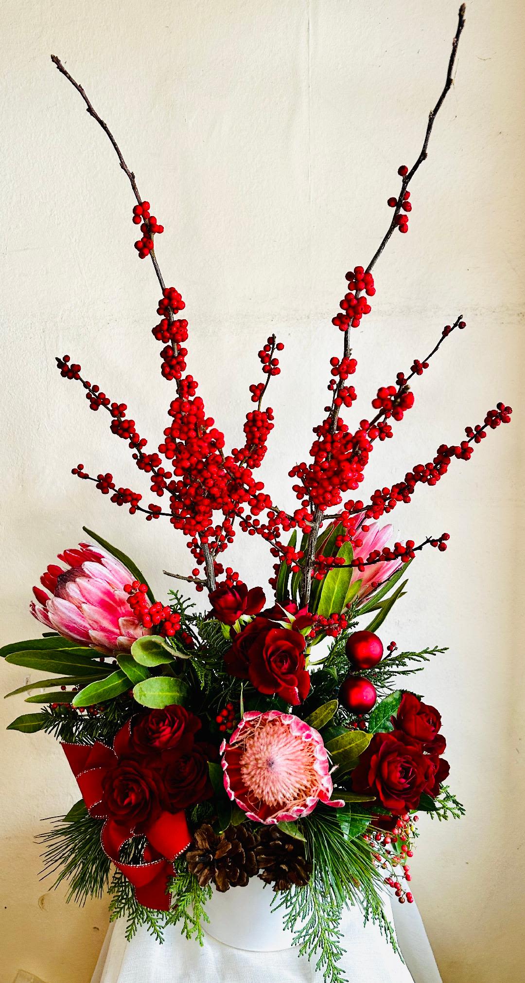A very Berry Merry Christmas - Towering Ilex berries, textured protea, red roses, lush greenery decorated for Christmas in a ceramic vessel. 
