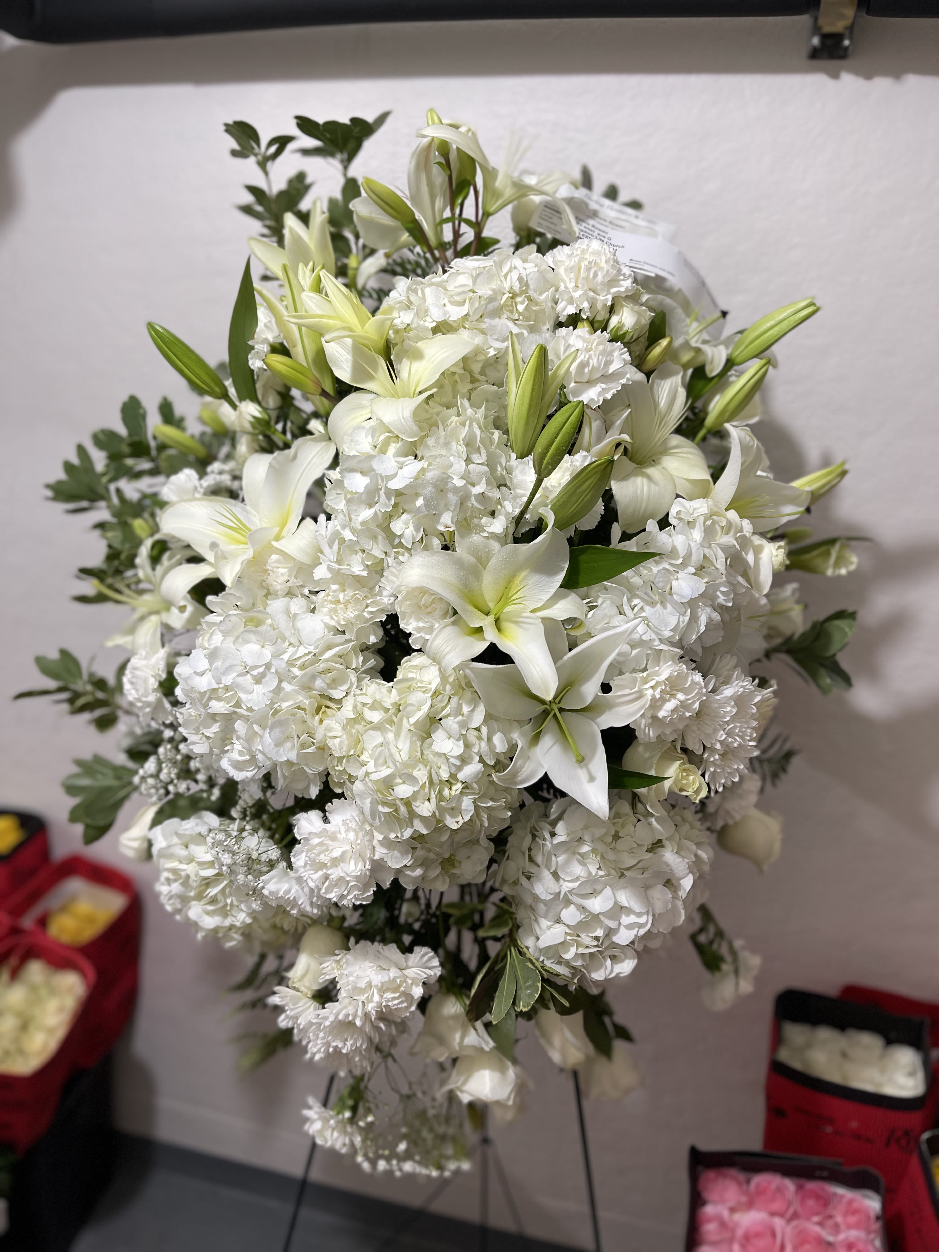 White Christmas Standing spray  - White Christmas Standing Spray Honor the season with a graceful tribute of winter beauty. This stunning standing spray blends snowy white blooms—such as lilies, roses, carnations, and seasonal accents—arranged in a sweeping, elegant display. Soft evergreens, frosted accents, and touches of holiday texture bring a peaceful Christmas feel, creating a heartfelt expression of love, remembrance, and serenity. Perfect for honoring someone special during the holiday season with purity, warmth, and timeless grace.