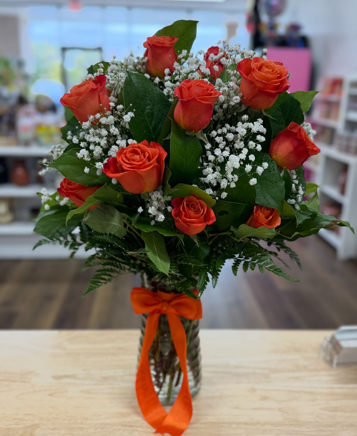 Orange Elegance - This stunning arrangement features a dozen premium orange roses, complemented by delicate baby's breath and lush baker fern, all elegantly displayed in a tall, clear glass vase. Orange you glad you found this arrangment! 