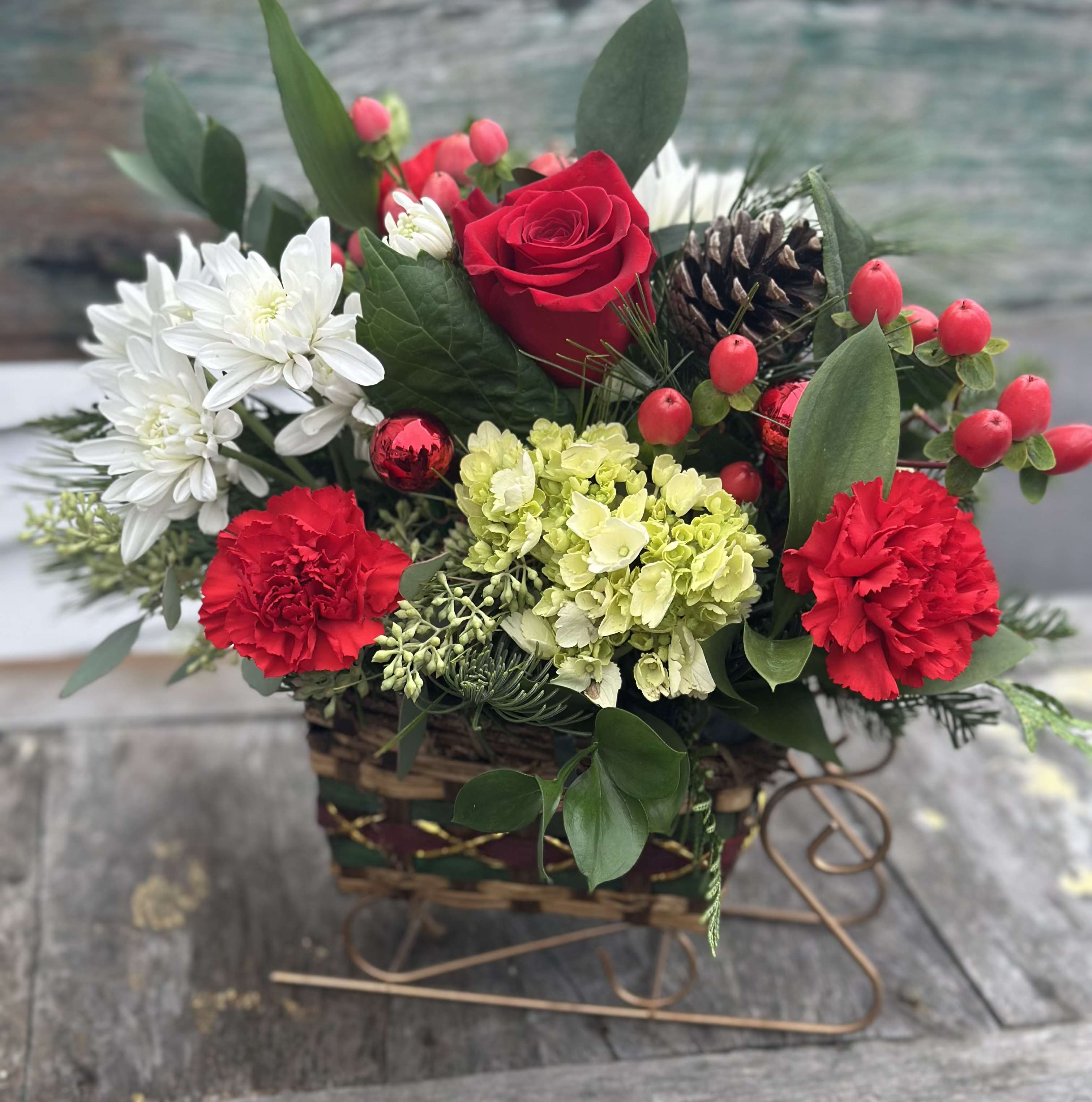 Sleigh Full of Cheer - A charming sleigh filled with red roses, carnations, red hypericum berries, green hydrangea, white chrysanthemums and pinecones.