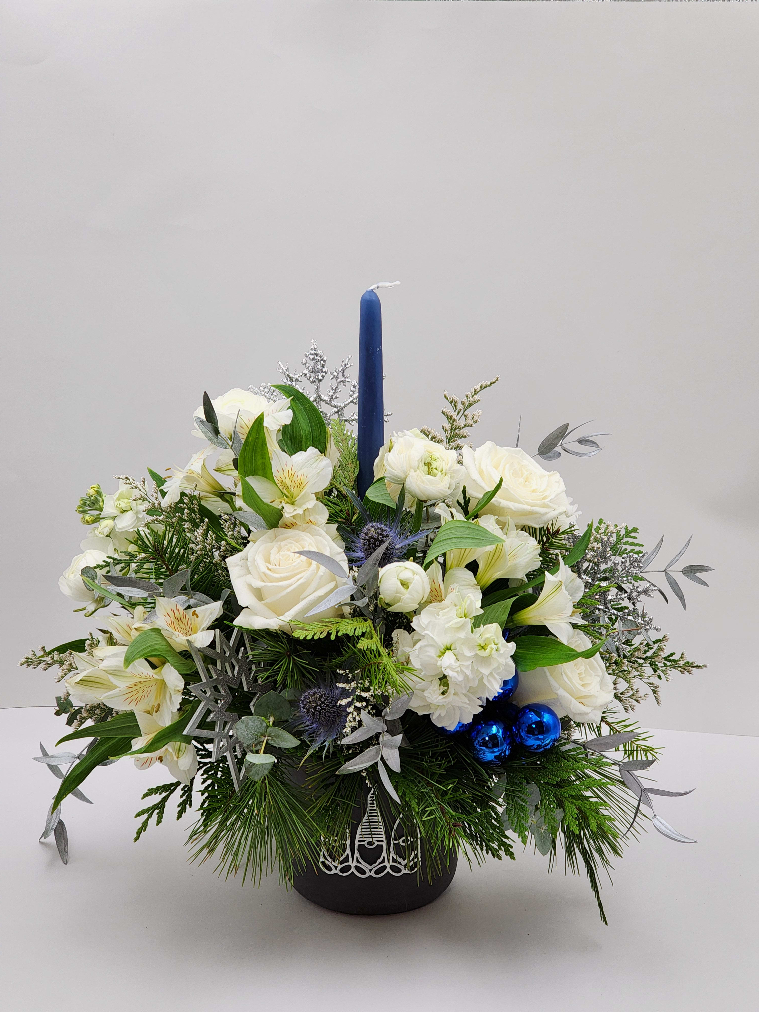 White Christmas - Select this unique centerpiece in a black gnome container that features a blue taper candle, roses, alstroemeria, ranunculus and more! Approx. 17&quot;W x 17&quot;H