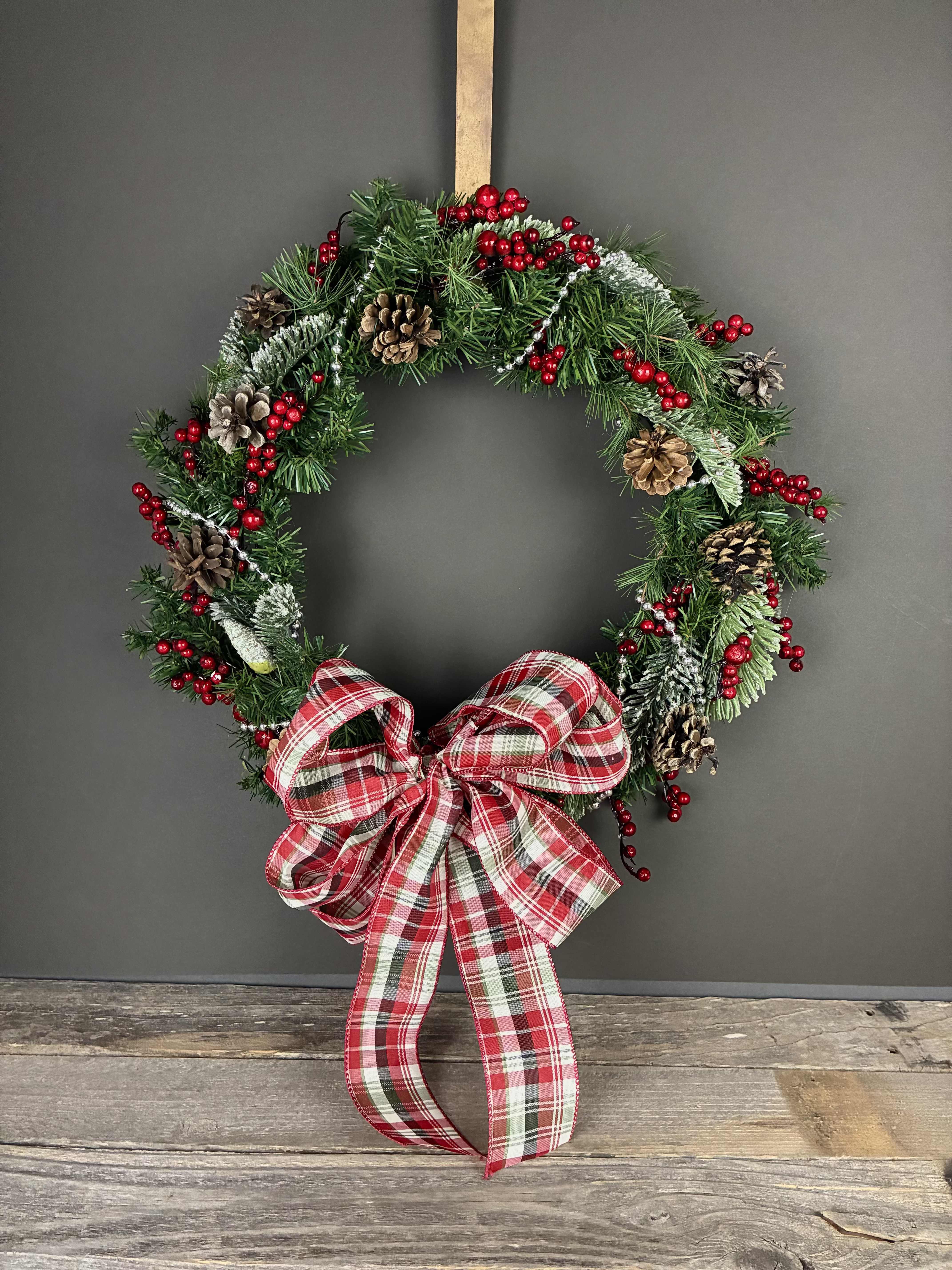 Merry Berries Wreathe - Celebrate the holidays with this one of a kind wreathe featuring red berries, pine cones, silver beads and a big plaid bow!  Measurements: 17in across All of our wreathes are hand made by our designers and we never make the exact same wreathe twice! If you would like a wreathe similar to this one, please call or email the shop.