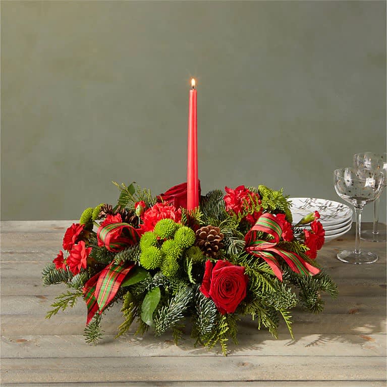 By the Candlelight Centerpiece - Let time fly By the Candlelight centerpiece as new holiday memories are made. What better way to commemorate the joyful homecoming than with classic red roses and lush evergreen accents?  Please Note: The bouquet pictured reflects our original design for this product. While we always try to follow the color palette, we may replace stems to deliver the freshest bouquet possible, and we may sometimes need to use a different vase.