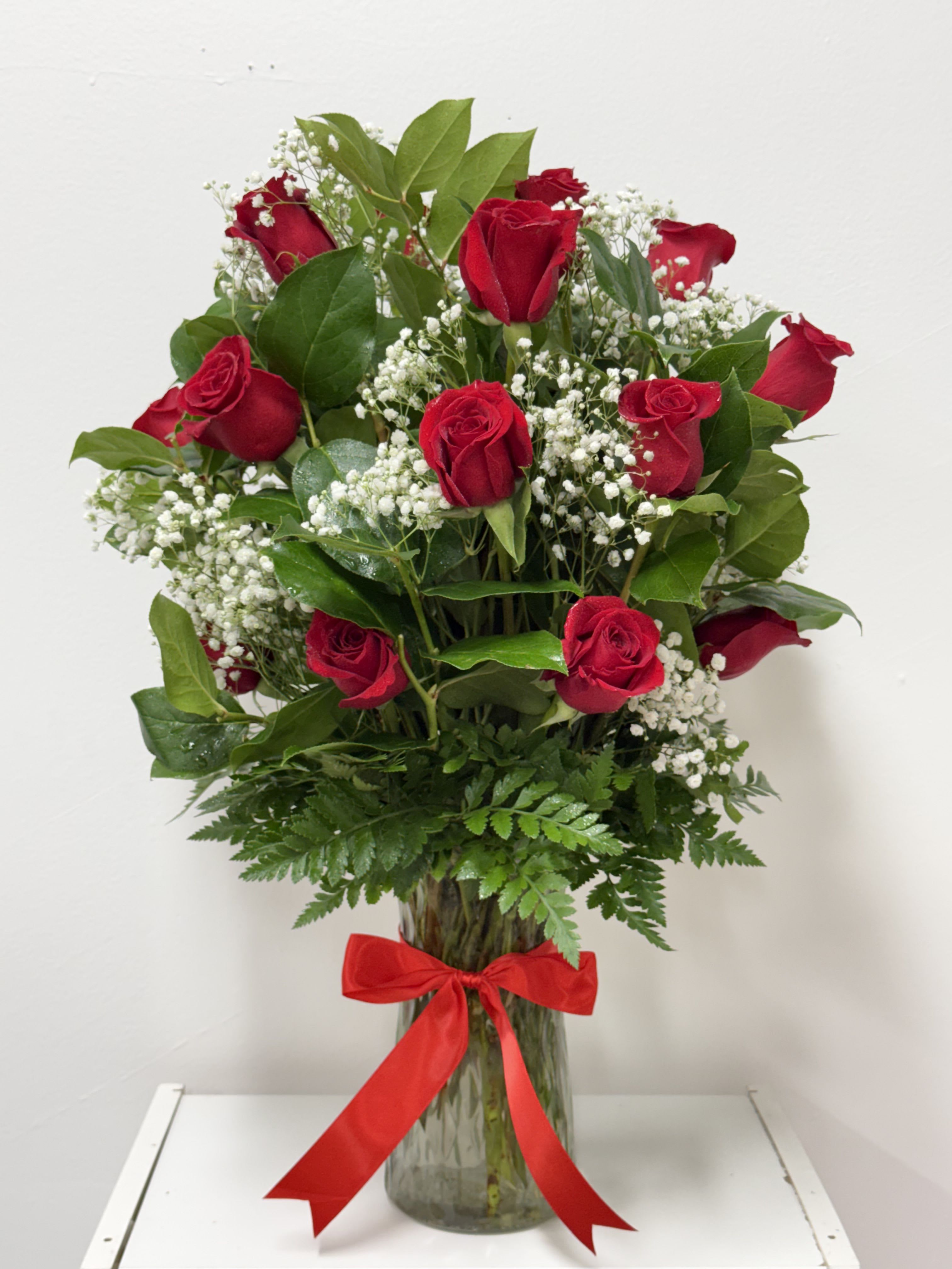 Timeless Grace - This stunning bouquet features a dozen premium red roses, complemented by delicate baby's breath and lush greenery, all elegantly displayed in a tall, clear glass vase. Perfect for romantic gestures, special occasions, or simply to add a touch of elegance to your home, this arrangement exudes sophistication and charm. 