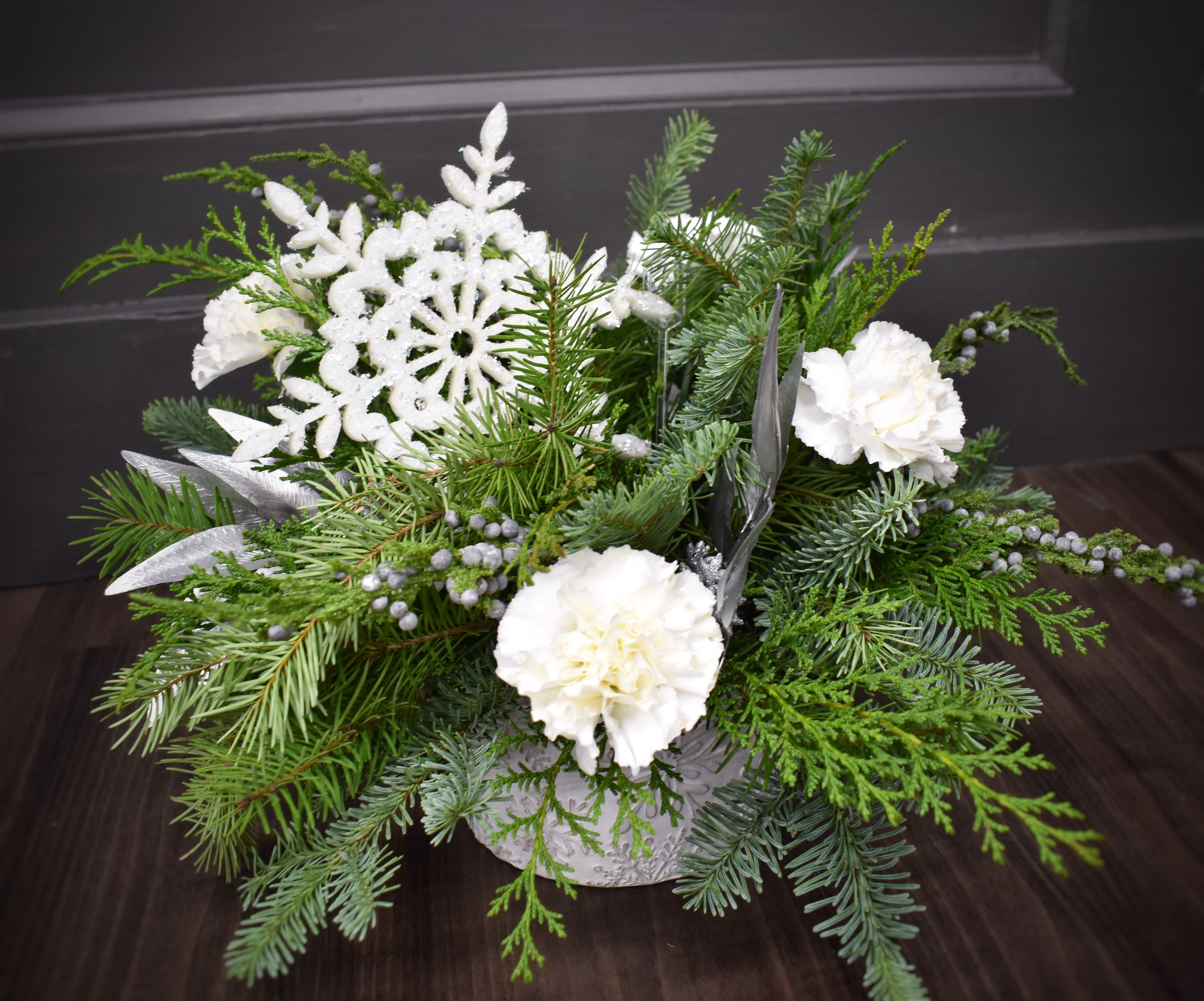 Winter White Snowfall - Just like a gentle snowfall, this arrangement is a beautiful sight to see! A large white snow flake nestled into a keepsake container filled with fresh winter greenery, fluffy white carnations and accented with silver silk leaves, and stems of everlasting juniper. 