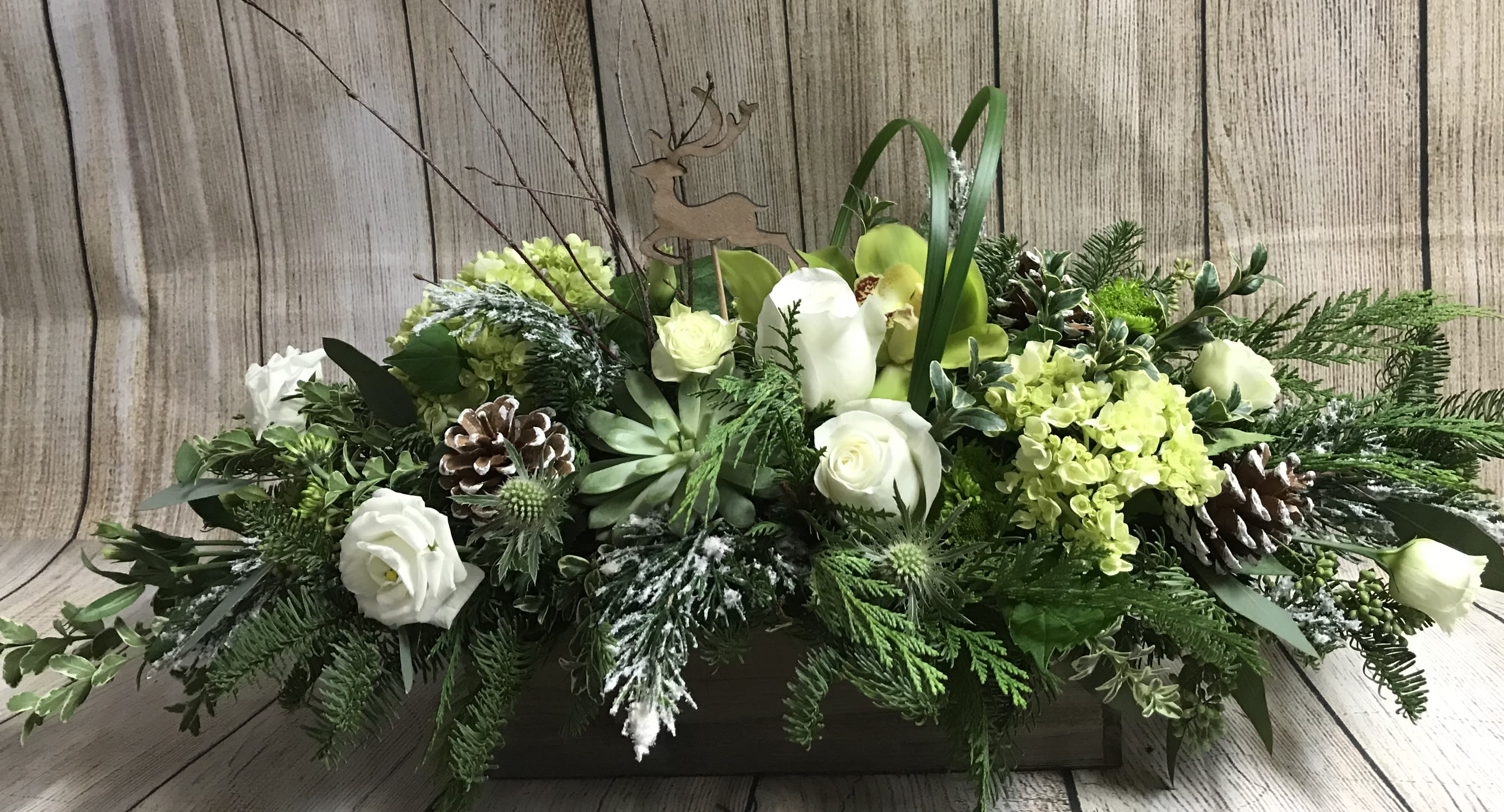 “VIXON” - A winter mix of assorted foliage, natural palette of roses, orchids, lisianthus, pine cones, birch branches and a flying reindeer, all designed in a rustic wooden box.