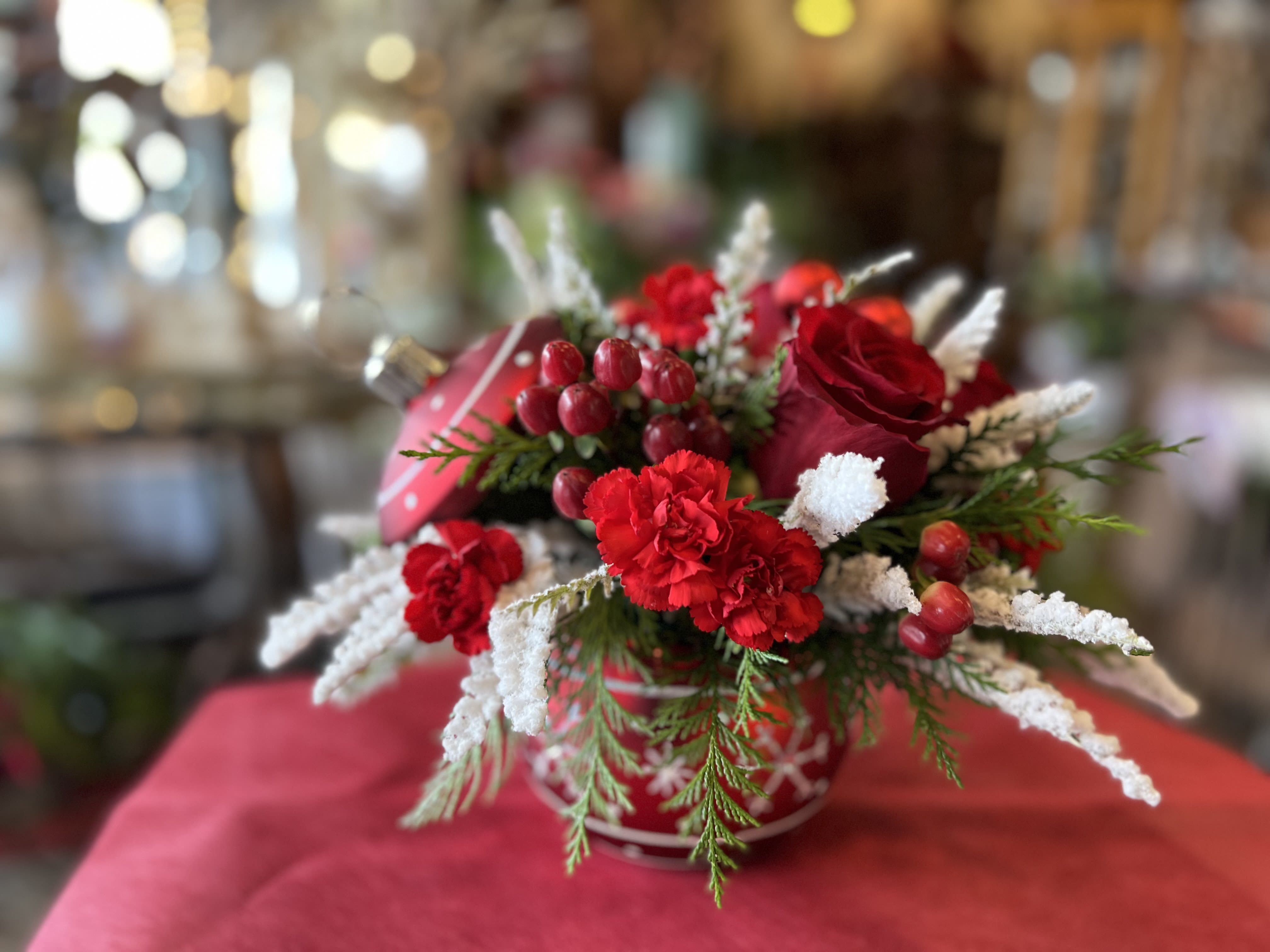 Snowflakes and Scarlet  - This arrangement features stunning red roses, red hypericum berries, mini carnations, frosted grevillea and cedar designed in an ornament vase. The perfect gift for this holiday season.