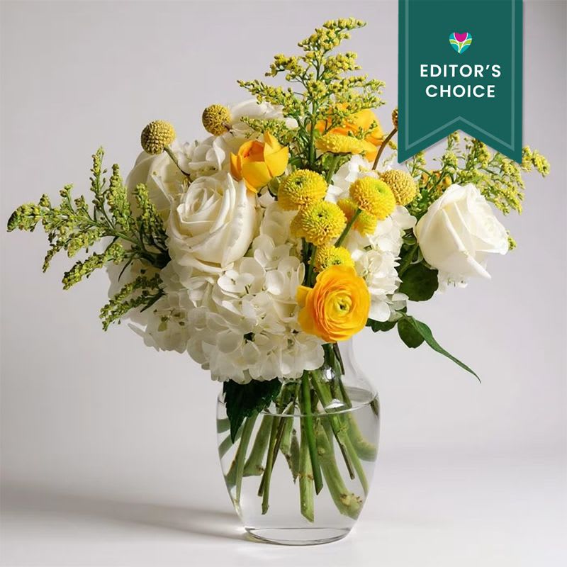 Little Miss Sunshine - Editor's Choice - Say hello to happiness! Little Miss Sunshine is a joyful burst of bright yellow blooms designed to bring instant smiles. With sunny yellow ranunculus, cheerful button mums, fun and funky billy balls, and fluffy white hydrangeas, this arrangement is pure sunshine in a vase. It’s bubbly, vibrant, and bursting with personality — the perfect way to brighten someone’s day, celebrate good vibes, or just sprinkle a little sunshine wherever it goes!      Vase subject to change