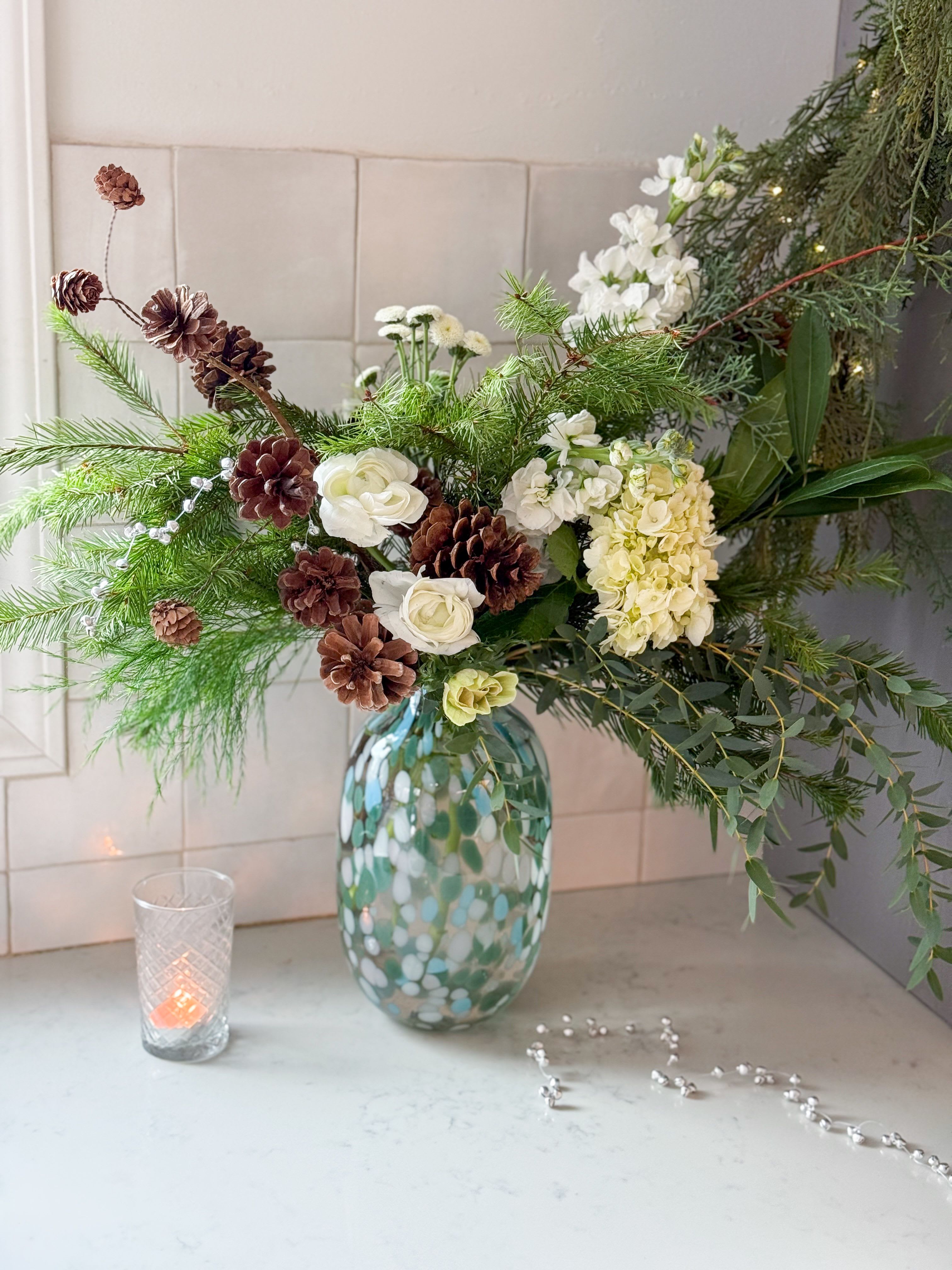 Noel  - A beautiful tall 10 inch painted glass vase designed with fresh holiday greenery white florals and pine cones.  