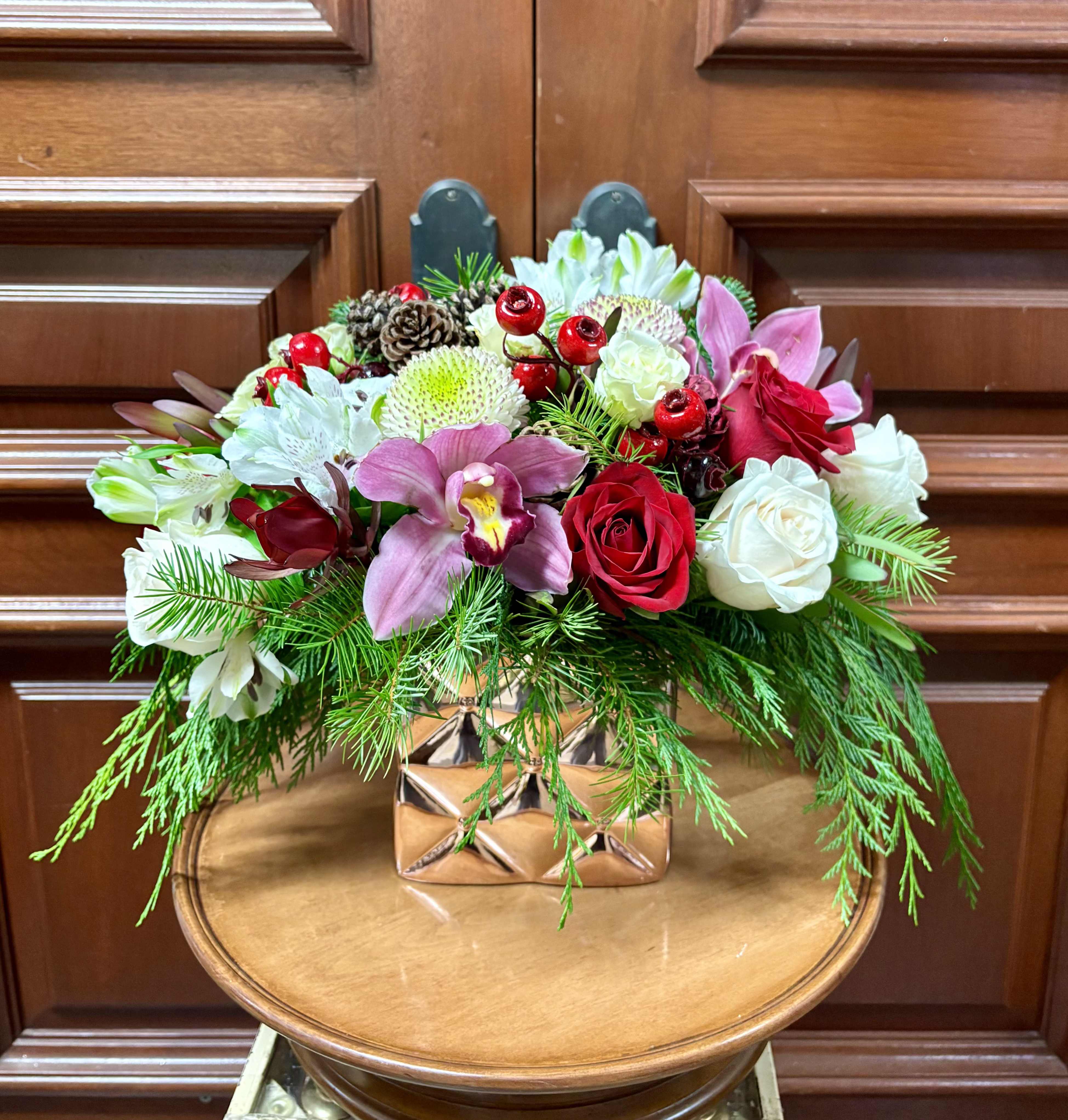 Winter is Here - Perfect for winter brithdays! Recipe: White Mums, White and Red Roses, Orhcids, Spray Roses, Alstromerias, Red Berries, and pine cones in a rose gold, square vase. Seasonal: All year round Orientation: All Facing View Photo shown: Standard