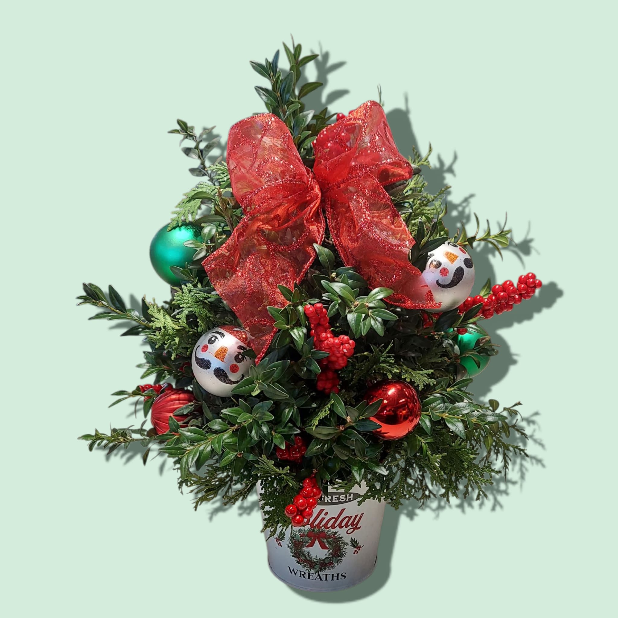 Christmas Boxwood Tree - The Christmas Boxwood Tree makes a festive addition to every holiday table. Fresh cut winter greens are adorned with bulbs and bows and presented in a holiday tin. The DELUXE version includes red carnations and white mums. COLOR OF TIN  AND BULBS WILL VARY. Approximate size: 17&quot;H x 12&quot;W