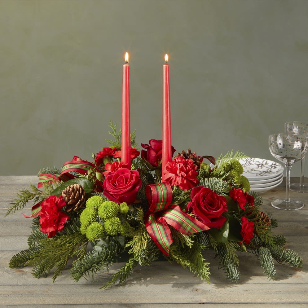 By The Candlelight - By the Candlelight centerpiece graces the table as new holiday memories are made. What better way to commemorate the joyful homecoming of the holidays than with classic red roses and lush evergreen accents.  B5437d