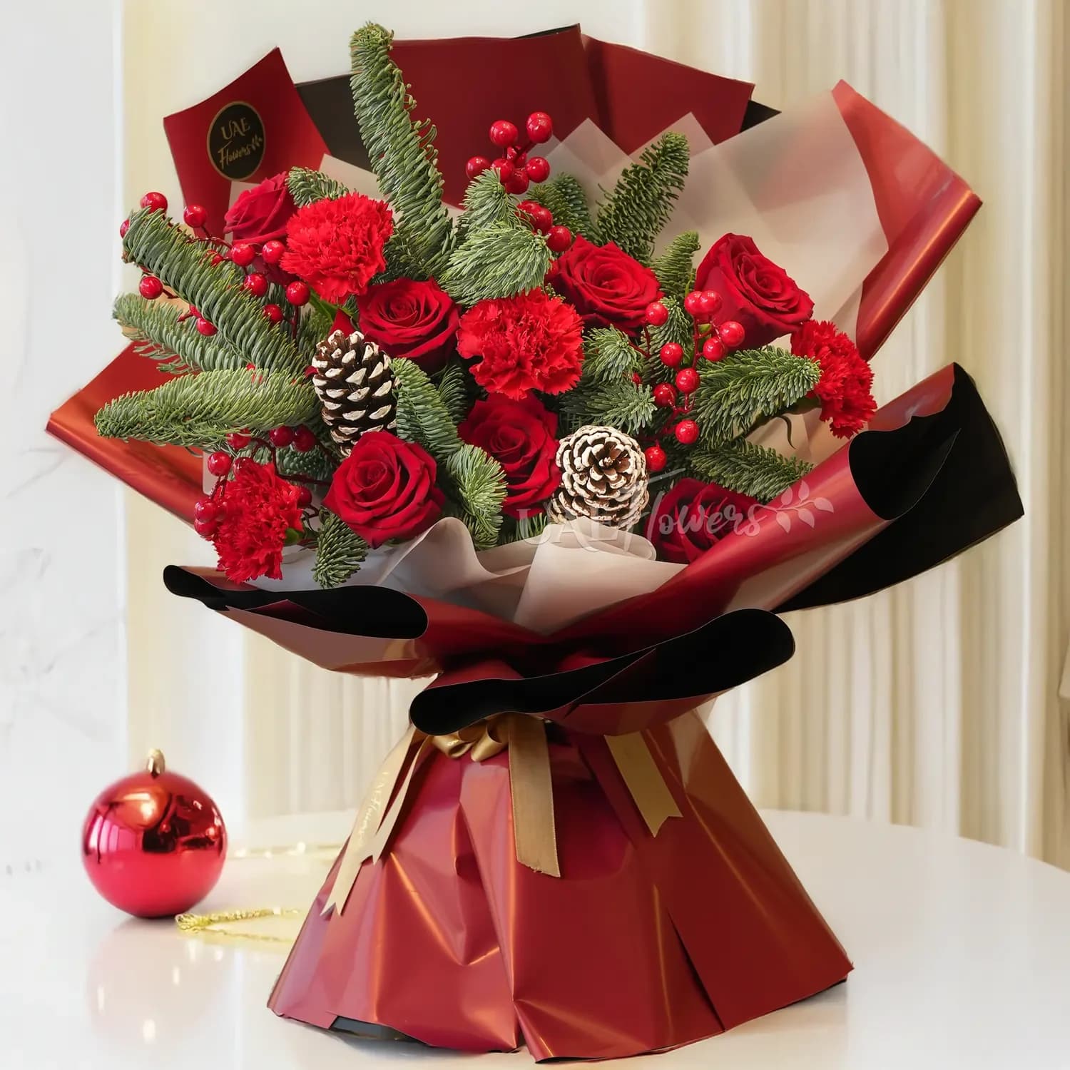 Classic Holiday Wrapped bouquet - This charming bouquet features a beautiful combination of red roses and red carnations, perfectly accented with rustic pinecones, vibrant hypericum berries, and fresh pine leaves. This arrangement blends romance with seasonal elegance, making it ideal for holiday celebrations, winter gifting, or heartfelt gestures.