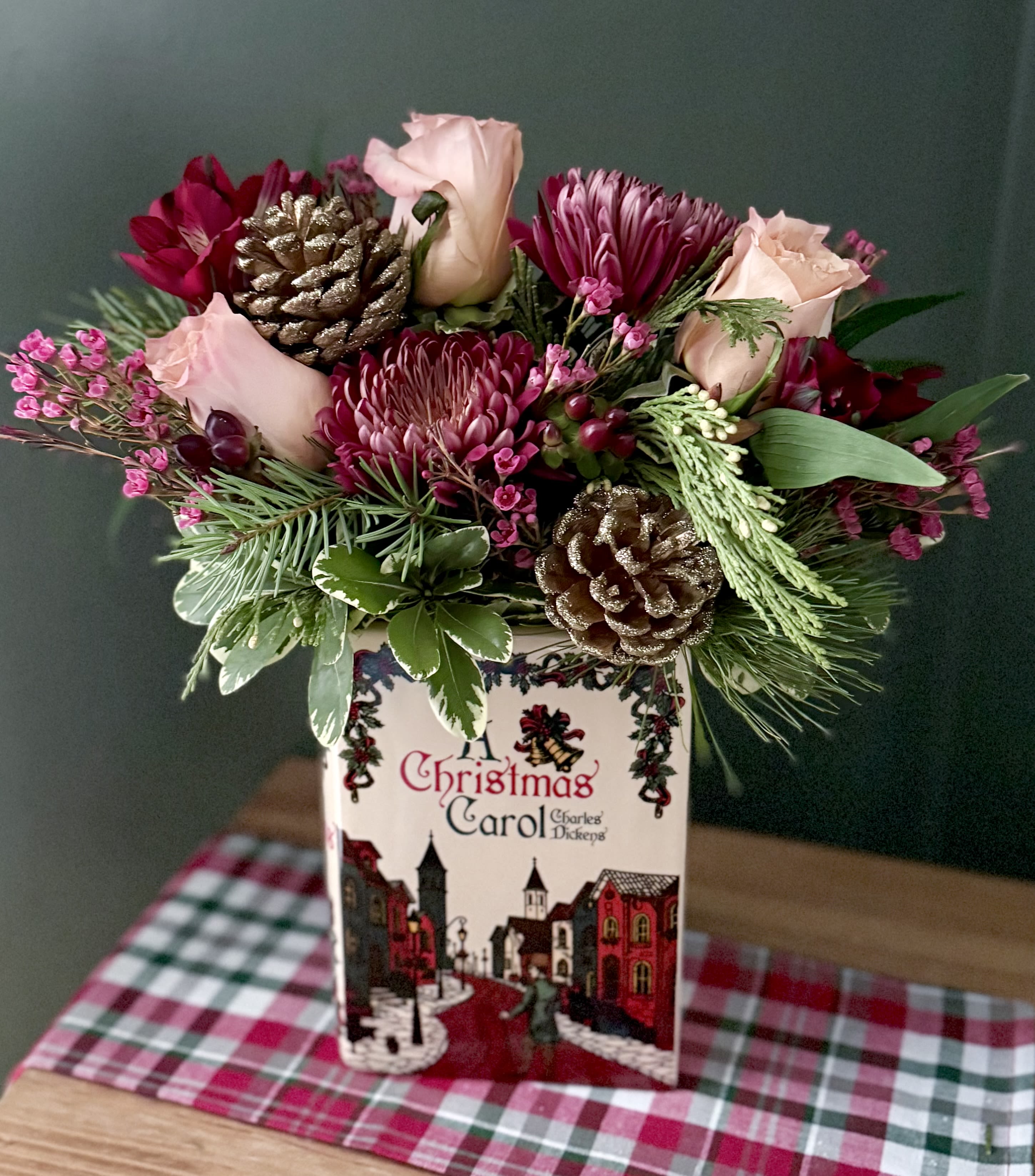 A Christmas Carol Book vase  - A ceramic vase in the shape of a book featuring a Christmas Carol! Filled with dark red cremons, berries, peach roses and gold sparkle pine cones. 