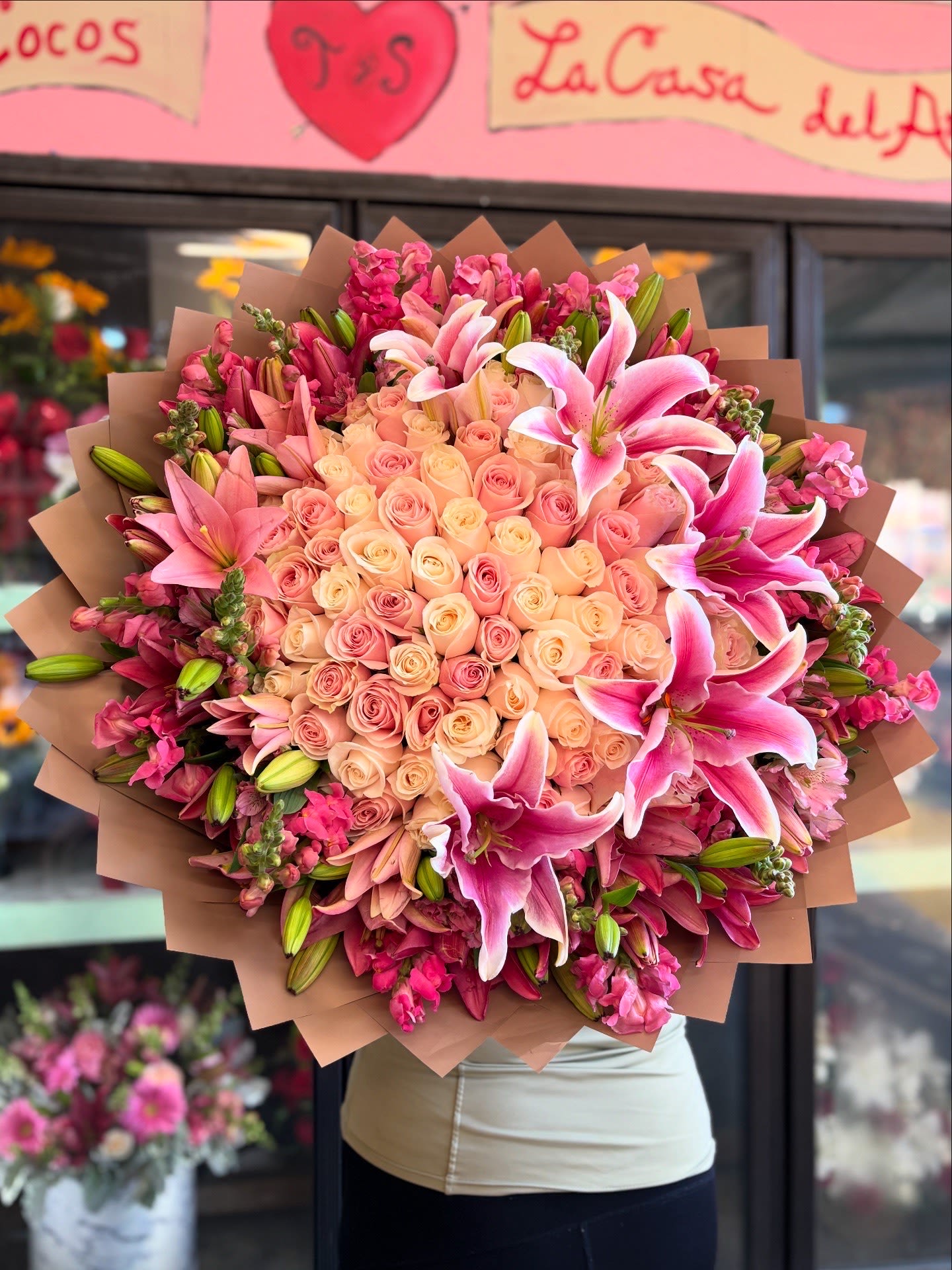 Stargazer Lily Luxe Buchon  - Go grand with this stunning 100-rose buchón, designed with 50 white roses and 50 pink roses, creating a perfect harmony of softness and elegance. Surrounding the heart of this arrangement are 20 lush lily stems, each with multiple buds ready to bloom...adding movement, fragrance, and dimension.  Intertwined with graceful snapdragons and alstroemeria the bouquet is wrapped in rich, coffee-toned paper, giving it a polished, modern finish.  To complete the statement, 5 oversized luxury lilies crown the bouquet, creating a larger-than-life look that commands attention and celebrates beauty on a grand scale.