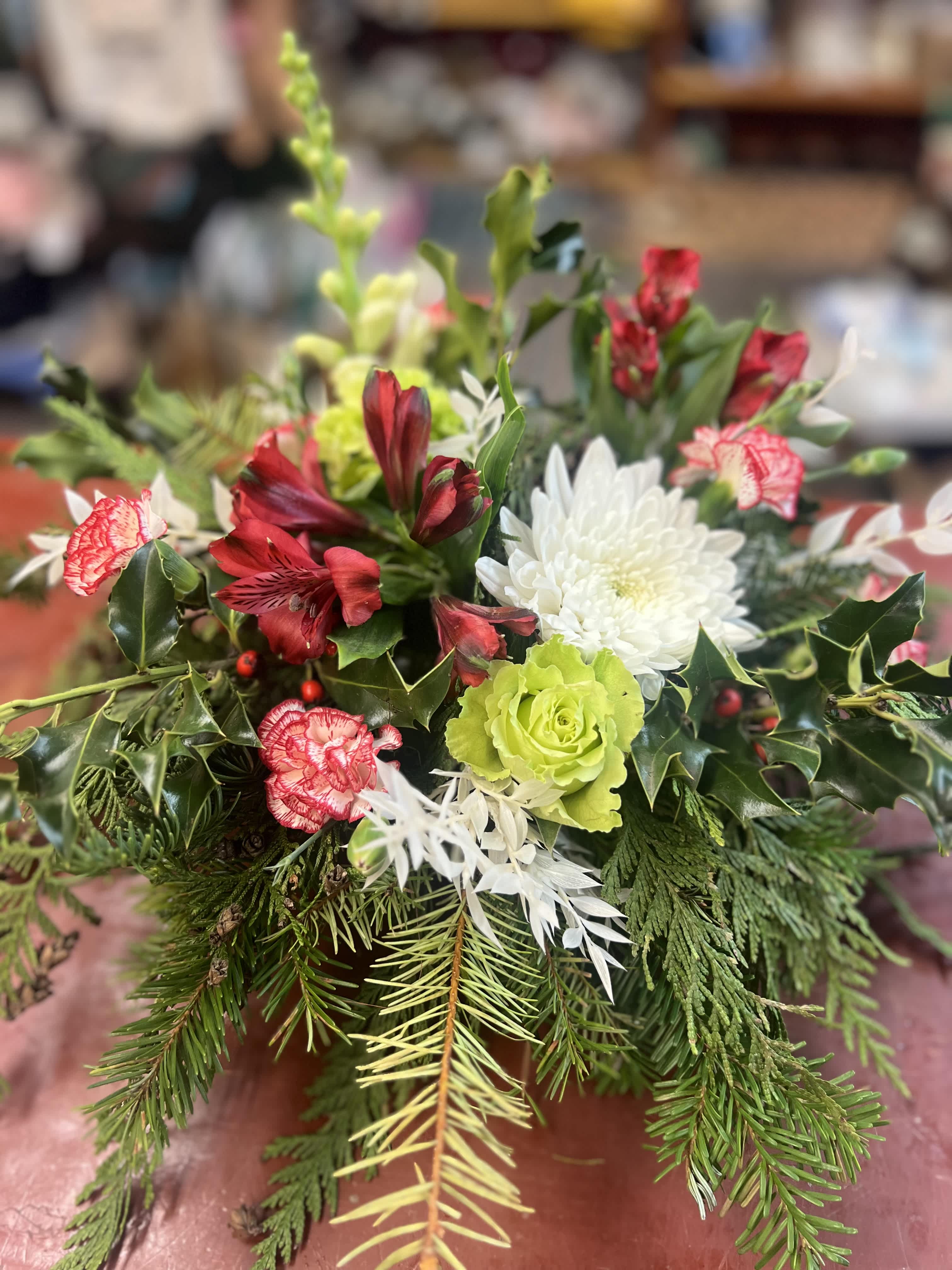 Christmas Gift Centerpiece  - Celebrate the season with a stunning holiday centerpiece crafted from fragrant evergreens, such as cedar and pine, paired with vibrant holiday-colored blooms and festive berries. Accented with a natural pinecone. This arrangement brings warmth, elegance, and the fresh scent of the season to your holiday table. 