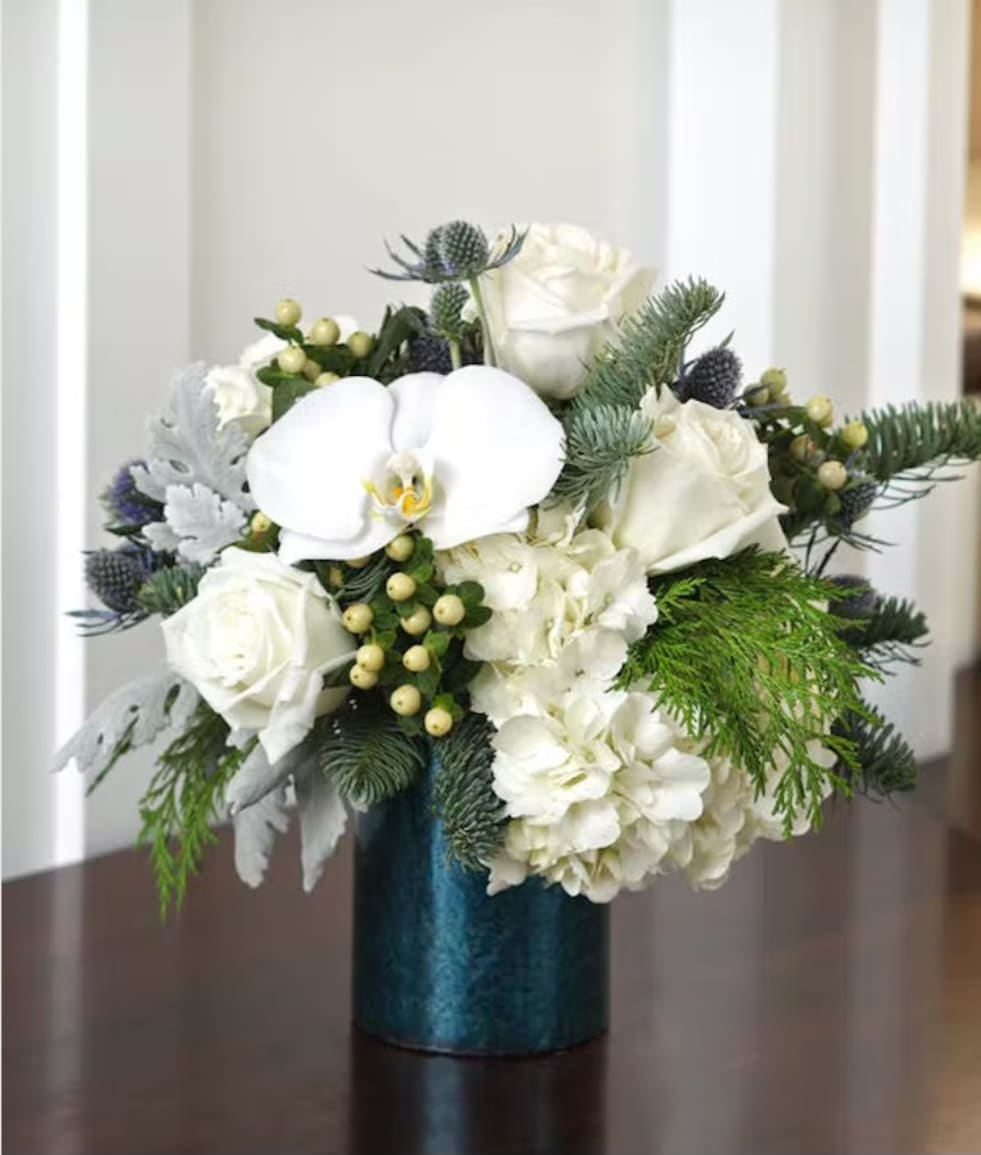 Lovely Blue &amp; White  - Our blue and white arrangement of fresh blue thistle, white roses,  white orchids, dusty miller and mixed winter evergreens, filled with seasonal white flowers expertly gathered together in a clear glass vase lined with decorative ribbon, makes for an exquisite gesture of any occasion.  Pictured is premium size