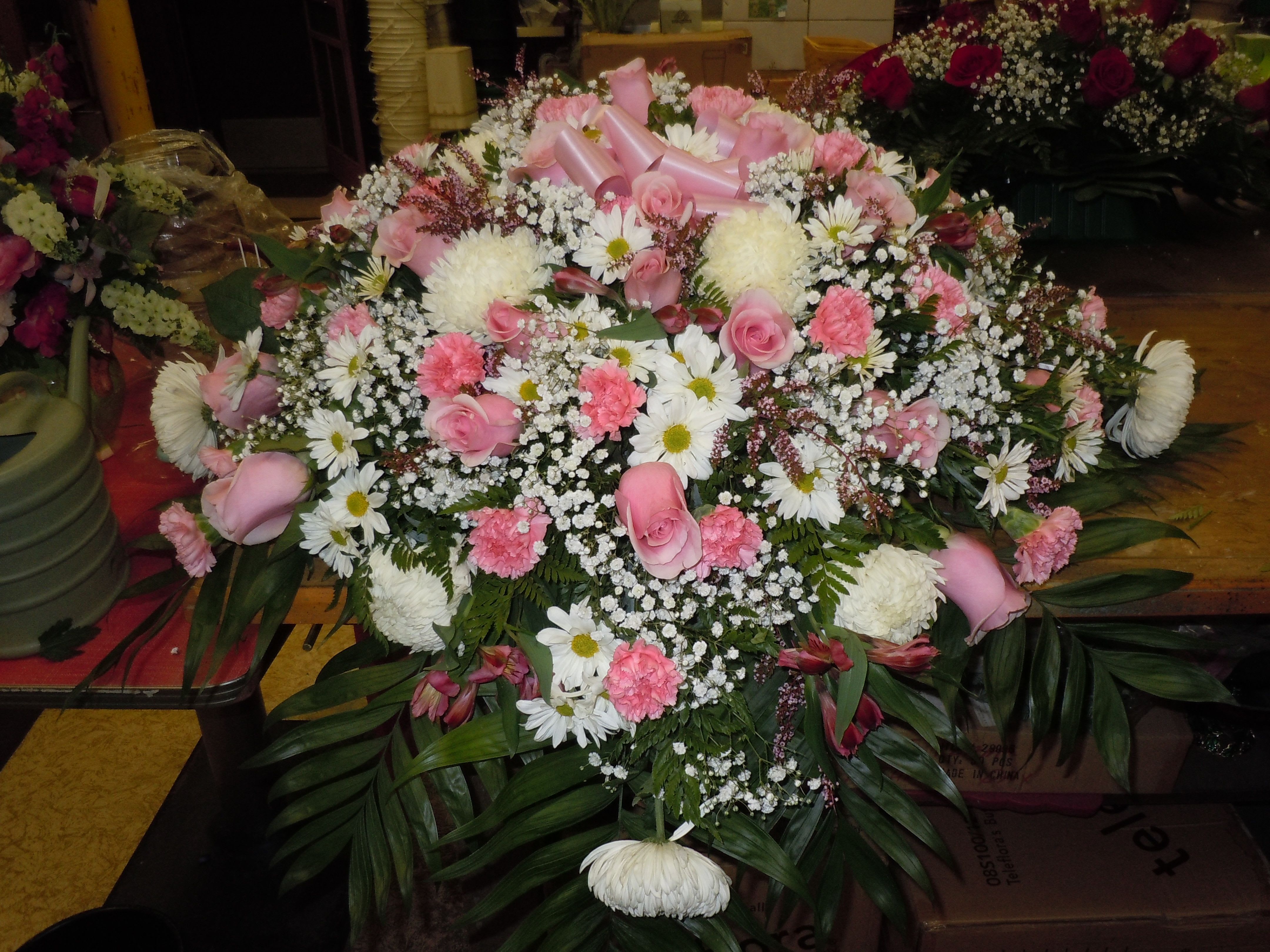 CASKET SPRAY - C19 - A mixture of white fuji mums, pink roses, pink carnations, white daisies, pink heather, pink alstro, greens, and baby's breath.   Banner - $15.00 + extra  Substitutions may apply, pending flower availability.