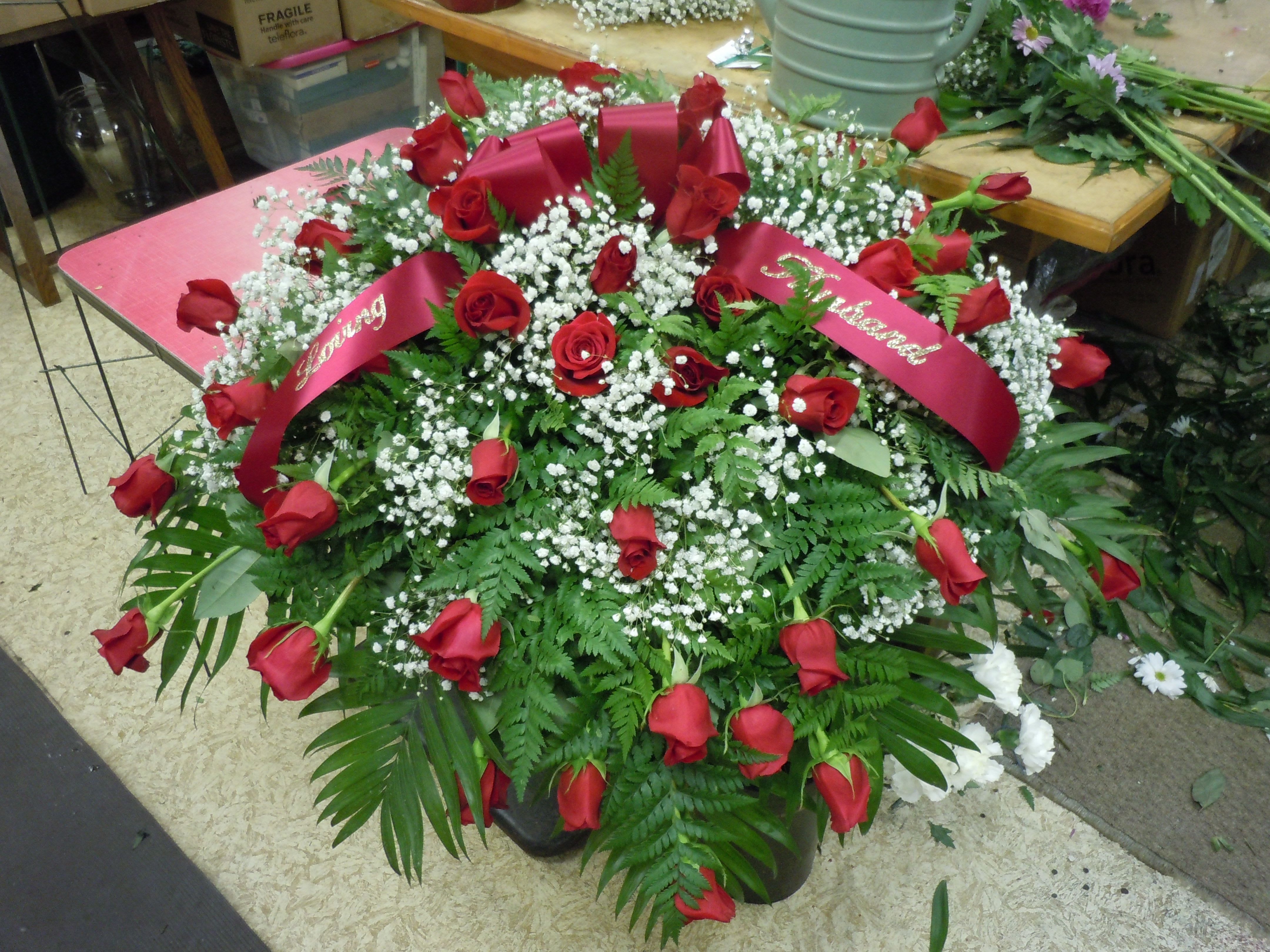 CASKET SPRAY - C20 - All red roses, greens, baby's breath, includes  bow.  Banner - $15.00 + extra  Substitutions may apply, pending flower availability.