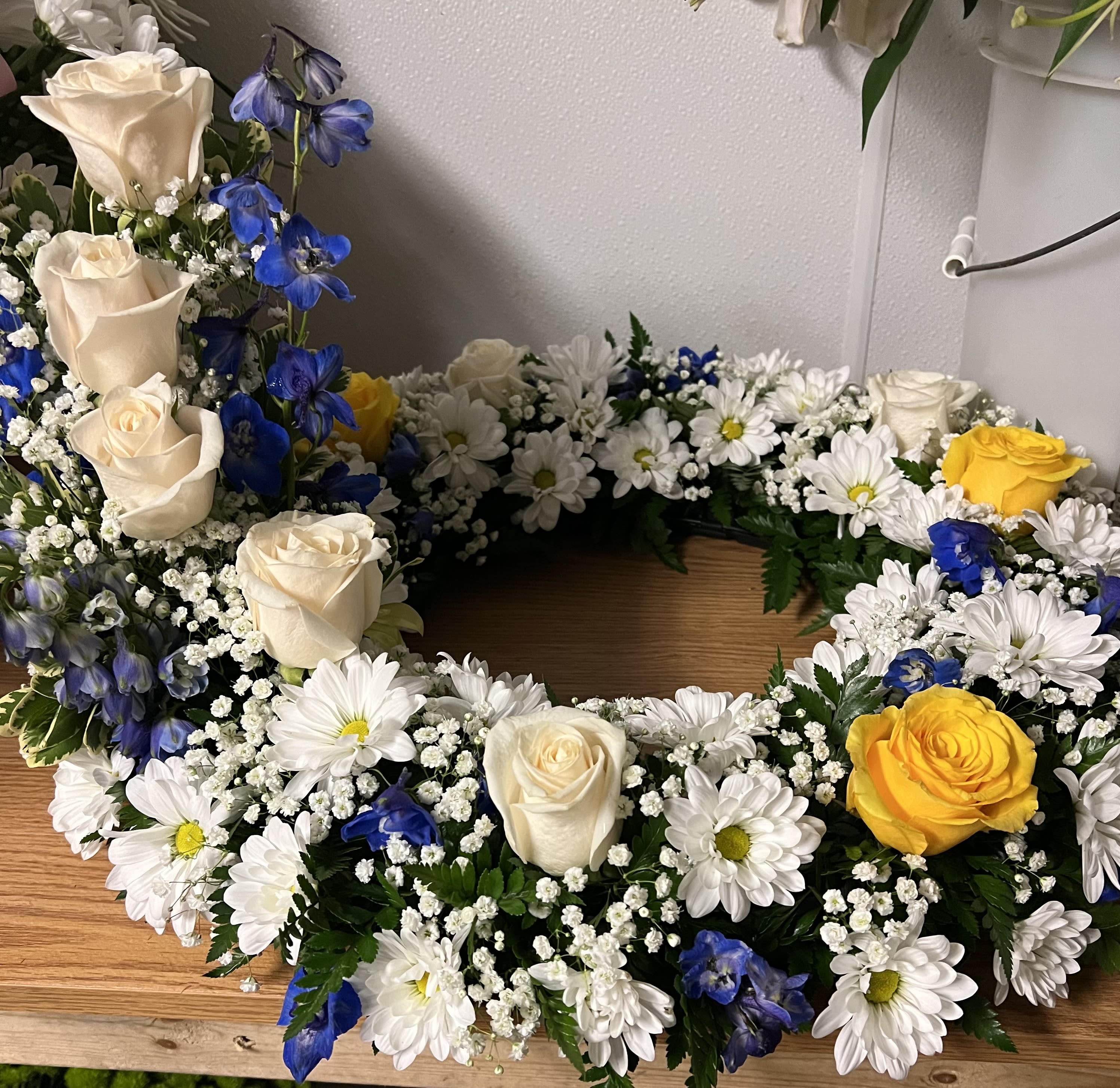Urn Wreath BW - Blue and white urn wreath including white roses , yellow roses and white daisies with blue delphinium and baby's breath