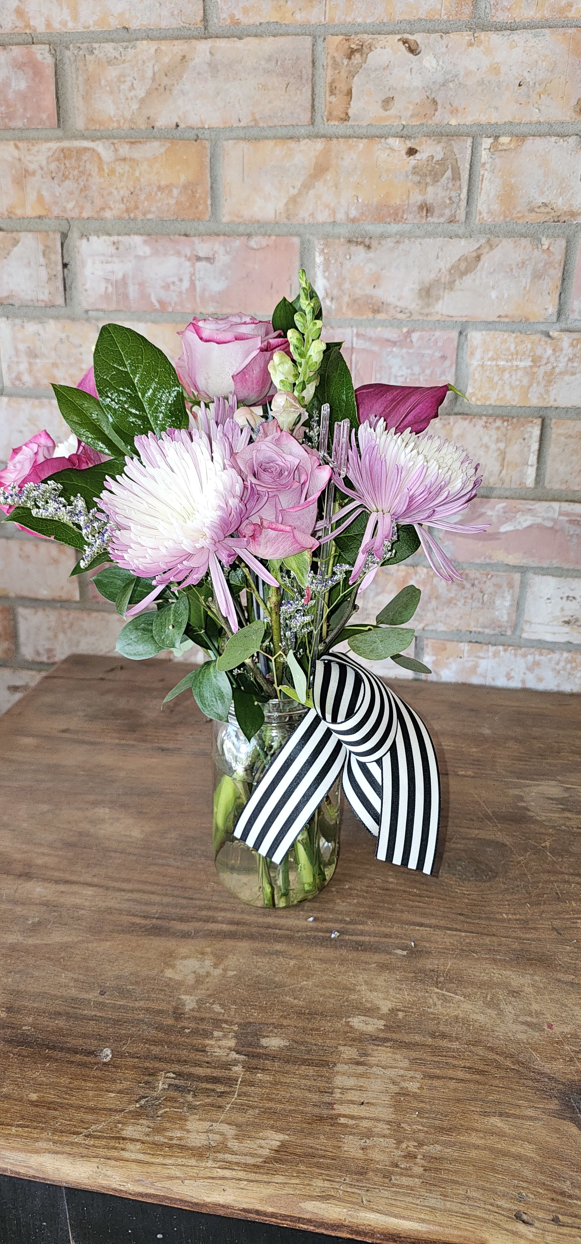  Farmers Market Jar - A Seasonal Mix in a cute mason style jar, full of premium blooms in the shades of spring like pink, lavender, yellow, and more!  A Signature Rose Soiree bow as the perfect finish. These make a great gift, and will fit perfectly on a desk , nightstand or vanity!