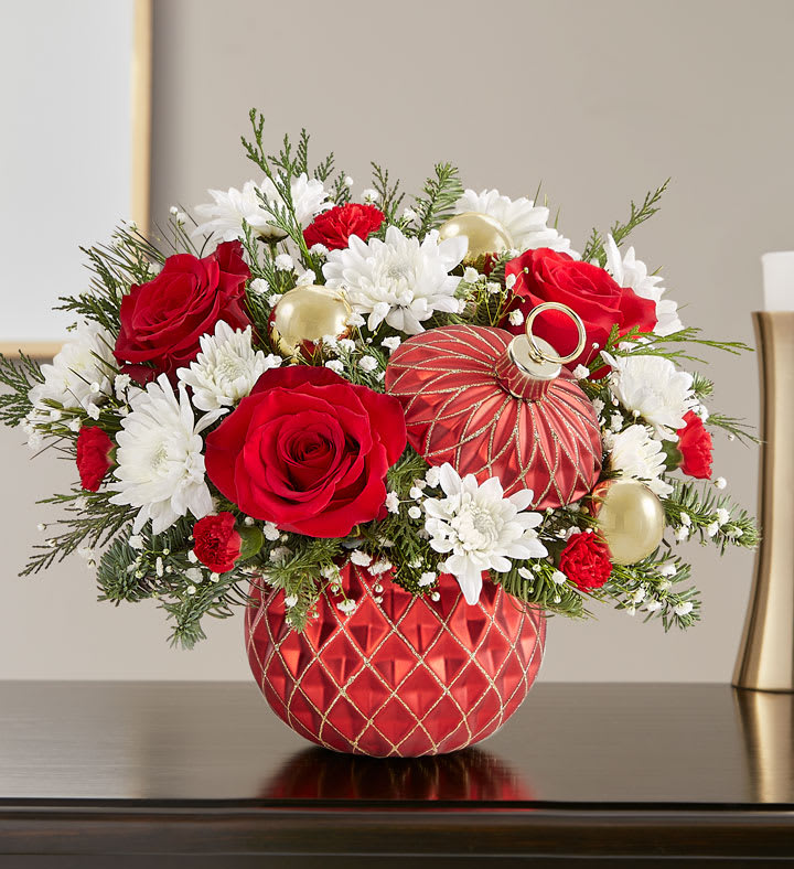 Sparkling Holiday Ornament™ - The signature beauty of the holiday season is captured in our limited-edition arrangement. Joyful red &amp; white blooms are gathered with festive gold ball ornaments and arranged in our Sparkling Holiday Ornament™ container. With its diamond-embossed design, lavish gold glitter and matching lid, it’s a luxurious keepsake they’ll treasure for years to come.  All-around arrangement with red roses and mini carnations; white cushion poms; accented with baby’s breath, assorted Christmas greenery and decorative gold ornament balls Artistically designed in our exclusive Sparkling Holiday Ornament™, coated in a red satin finish and featuring diamond-embossed detail and lavish gold glitter accents; removeable lid allows this keepsake container to be used as a functional holiday décor piece after the floral has expired Our florists hand-design each arrangement, so colors and varieties may vary due to local availability