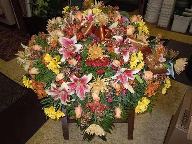 C7 Casket Spray - A mixture of terra cotta color fuji mums, shocking lilies, orange roses, burgandy, yellow and  orange daisies, burgandy alstro, orange wax flower, and greens.    Banner - $15.00 + extra  Substitutions may apply, pending flower availability.