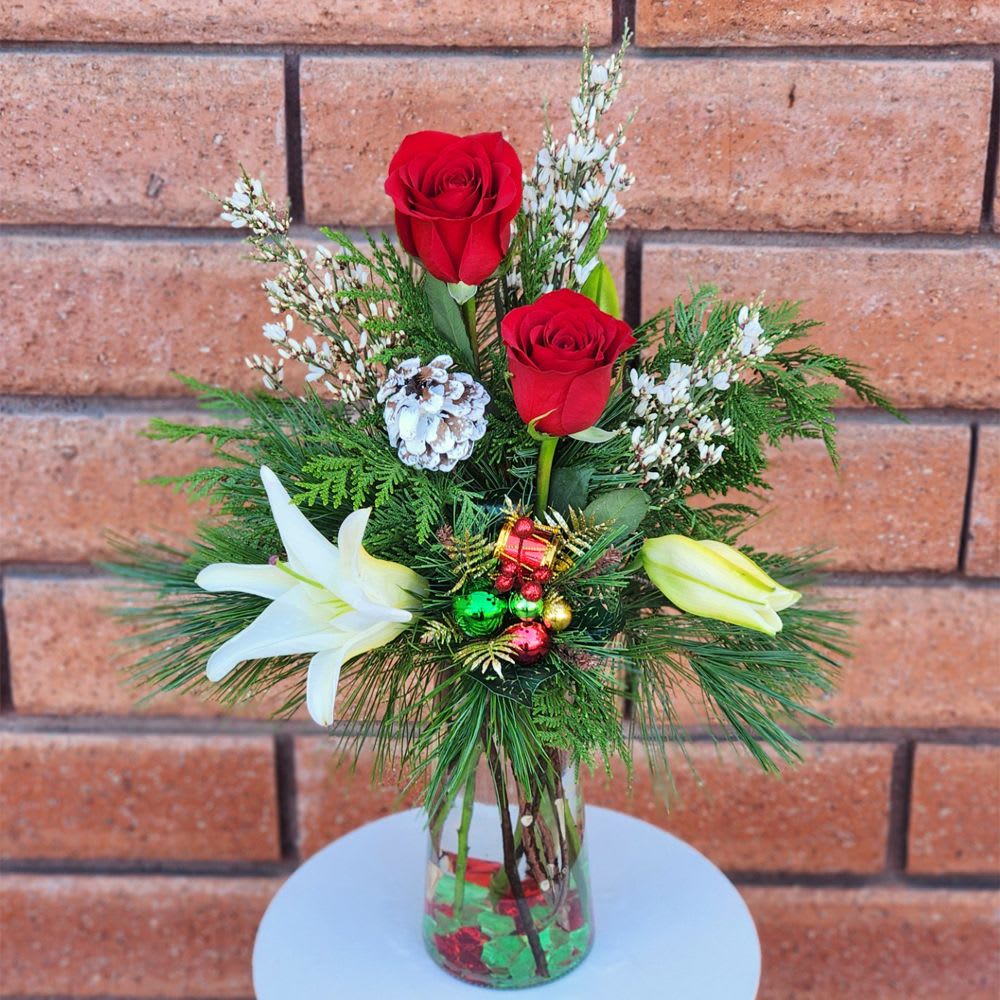 Home for Christmas Vase - Filled with fresh princess pine, western cedar, ornaments, pinecone and fresh cut flowers this lovely arrangement is worth bringing home. Standard size is approximately in (W) x in (H). Deluxe and Premium versions are larger and feature more premium blooms and larger vases.  Standard (Stem Count) - 2 Roses, 3 Genestra, 1 Crystal Blanca Lily, Princess Pine, Cedar and Decorations - Glass Vase  Deluxe (Stem Count) - 6 Roses, 4 Genestra, 2 Crystal Blanca Lily, Princess Pine, Cedar and Decorations - Glass Vase  Premium (Stem Count) - 9 Roses, 5 Genestra, 3 Crystal Blanca Lily, Princess Pine, Cedar and Decorations - Glass Vase  Care Tips: Place your bouquet in a cool location. Don't put the arrangement in direct sunlight, near heating or cooling vents, in drafty places, directly under ceiling fans, or on top of televisions or radiators. Check water level daily, keep the vase full of clean water. Change water every 2-3 days and apply a sharp fresh cut to the stems. This process will ensure extended flower's life span.