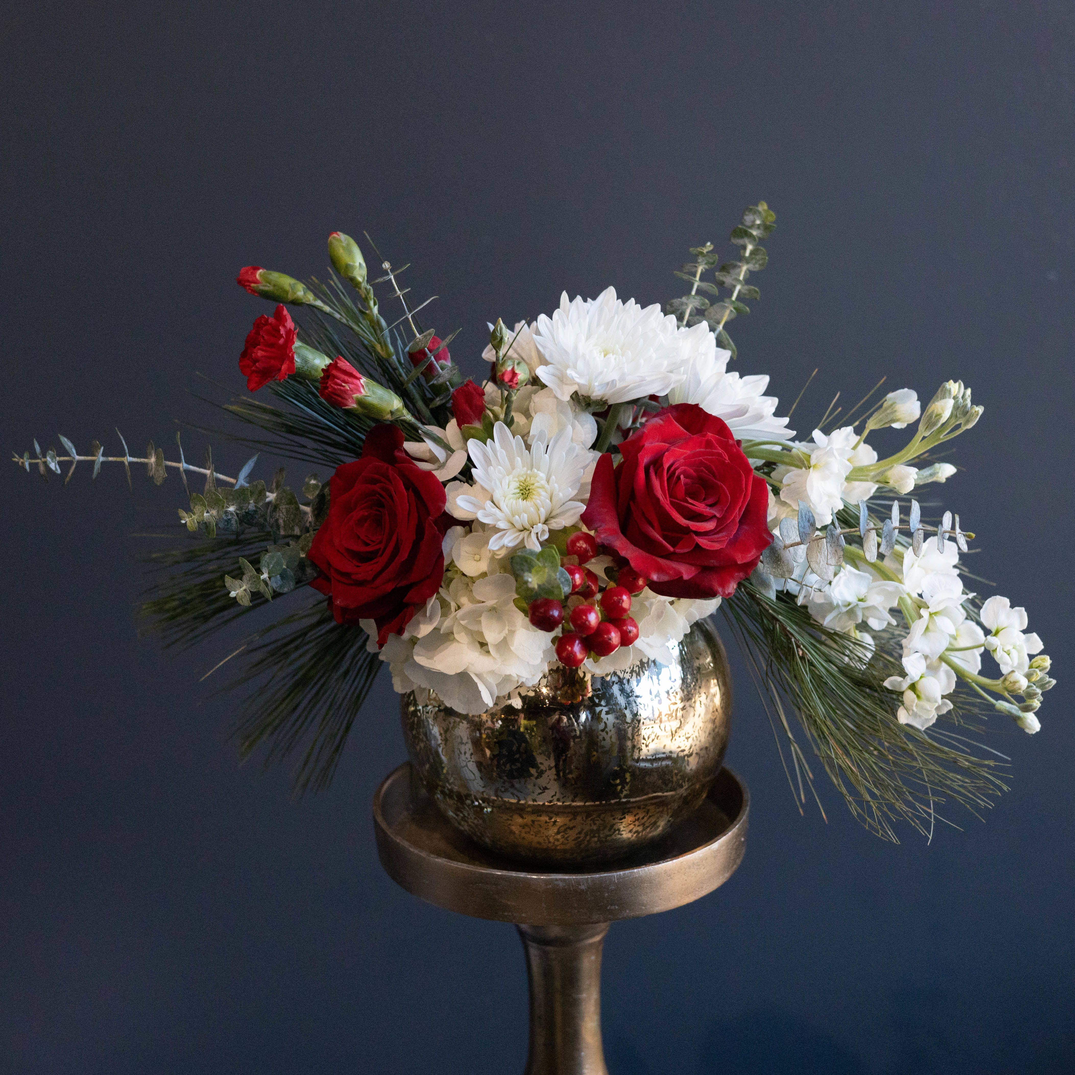 Noel -  This arrangement speaks to the elegant beauty of winter and the Christmas season. Featuring red roses and carnations, winter greens, white hydrangea, hypericum berries, and more.