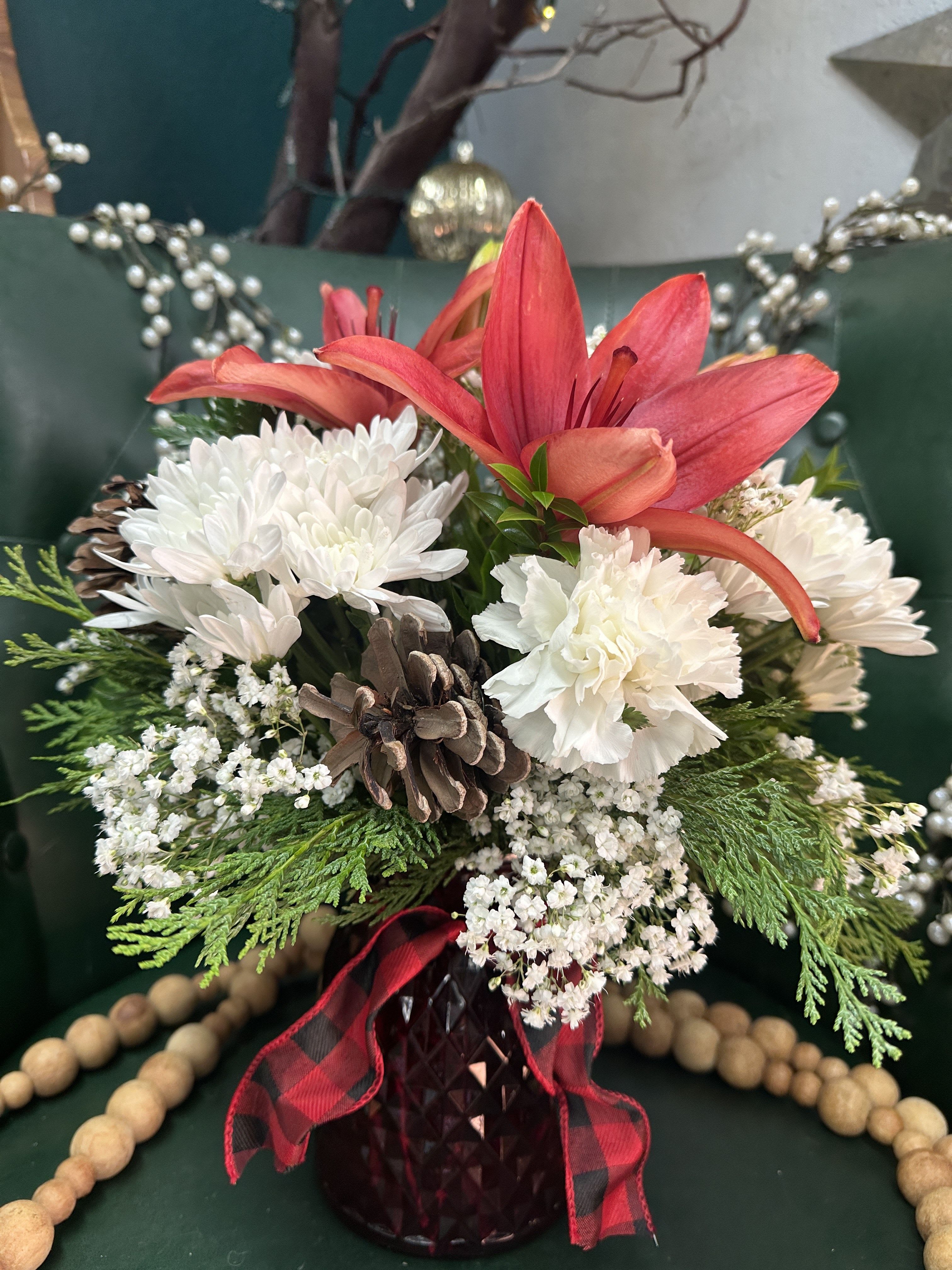 Buffalo Check Bouquet - Crisp whites carnations and chrysanthemums paired with warm red lilies show off beautifully in a red faceted vase. Finished off with a buffalo check sash and seasonal pinecones.   