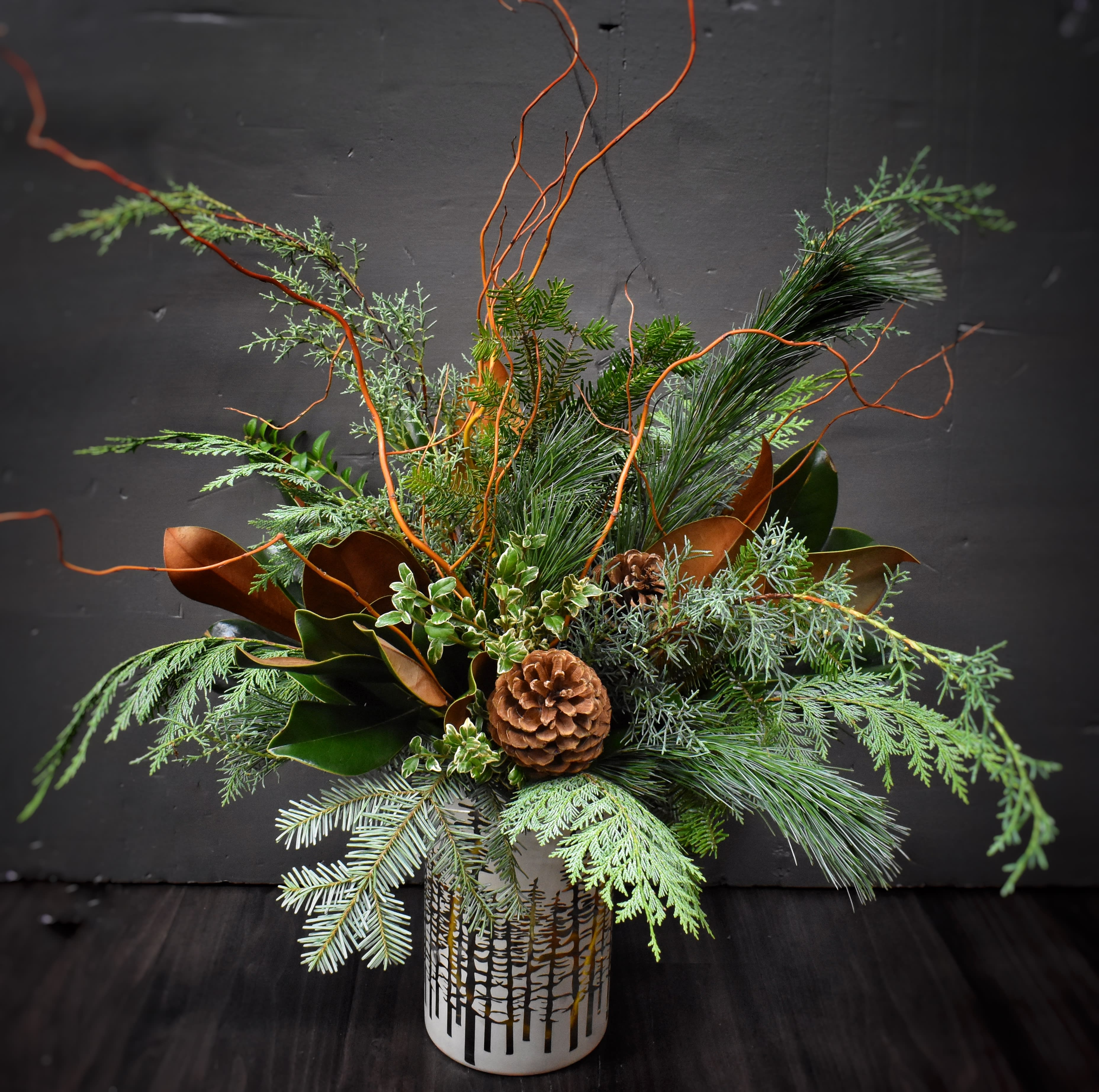 Finest Holiday Gathering - A large arrangement of seasonal greens and evergreens, branches, and pinecones in a beautiful gold and white hurricane container. 