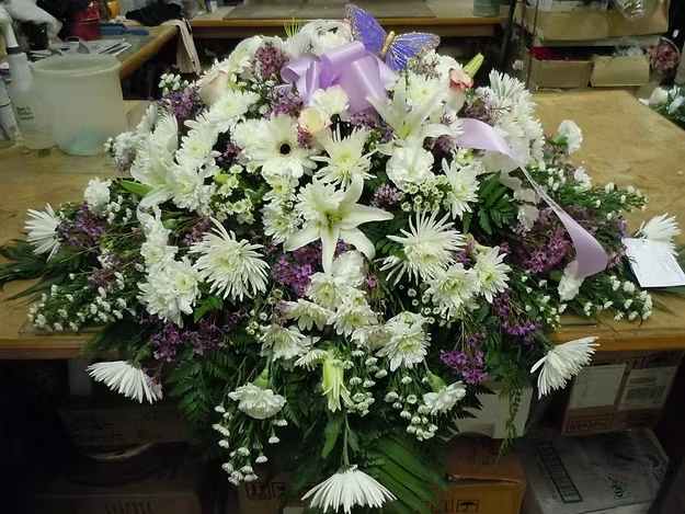 C10 Casket Spray - A mixture of white fuji mums, sweetness roses, white carnations, white cushion daisies, purple wax flower, white monte casino, and greens.  Includes  bow.  Banner - $15.00 + extra  Substitutions may apply, pending flower availability.