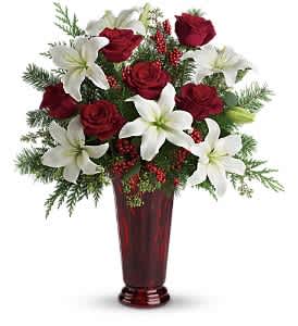 Holiday Magic - With beautiful red roses and brilliant white lilies delivered in a dramatic tall ruby vase, this dazzling holiday arrangement casts an enchanting spell. A step up from the traditional, its effect is nothing less than magical.