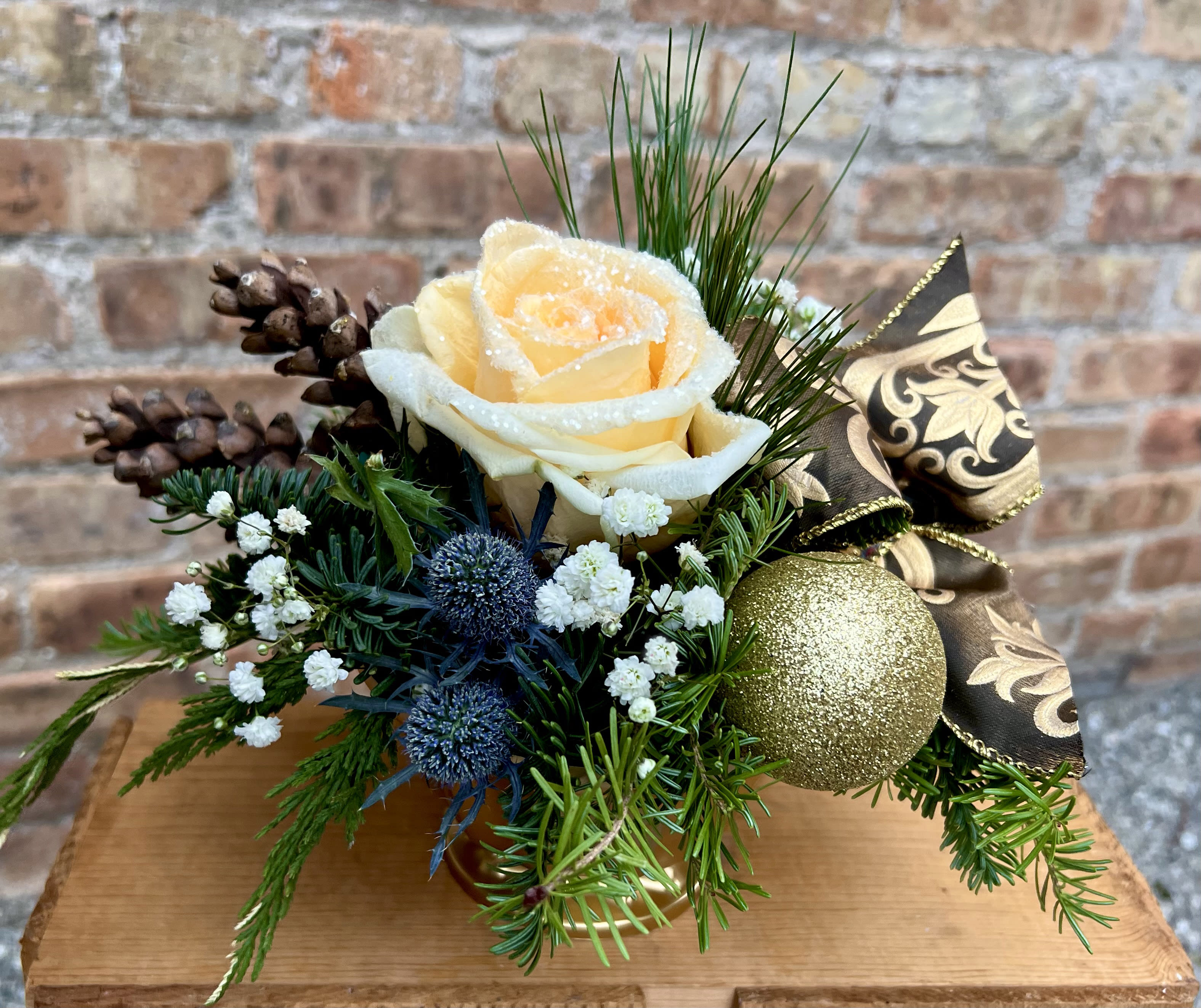 Golden Holiday - This adorable arrangement is the perfect size for a desk, coffee table or bedside table. A crystal glittered rose with ribbon, ornaments, thistle, pine cones, and winter greens all nestled in a small gold-toned container. Approximately 8"H x 10"W  We are proud to deliver our flower creations to the Kenosha, Somers, Bristol, and Pleasant Prairie area. With over 55 years of combined flower design experience in Kenosha, Wisconsin, A Summer's Garden Florist and Gifts is the perfect choice for the freshest flowers, most creative design, and exceptional customer service.