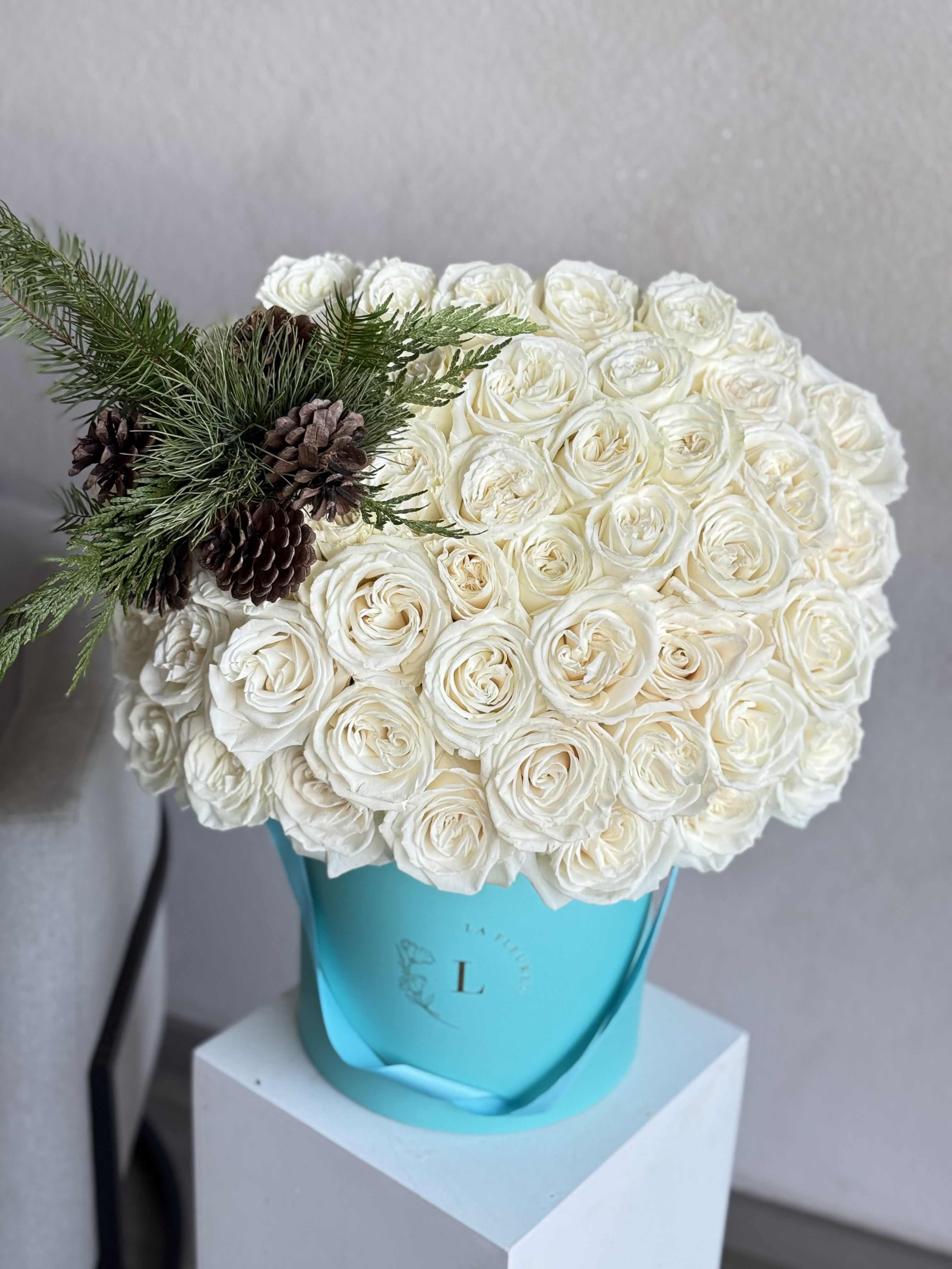 Winter Glow White roses arrangement - A luxurious winter statement, featuring 50 premium Playa Blanca white roses arranged with elegant seasonal greens. Designed to bring a soft holiday glow into any space, this long-lasting Christmas arrangement embodies purity, sophistication, and timeless celebration. Perfect as a festive centerpiece, a refined holiday gift, or a touch of winter elegance for the home or office.