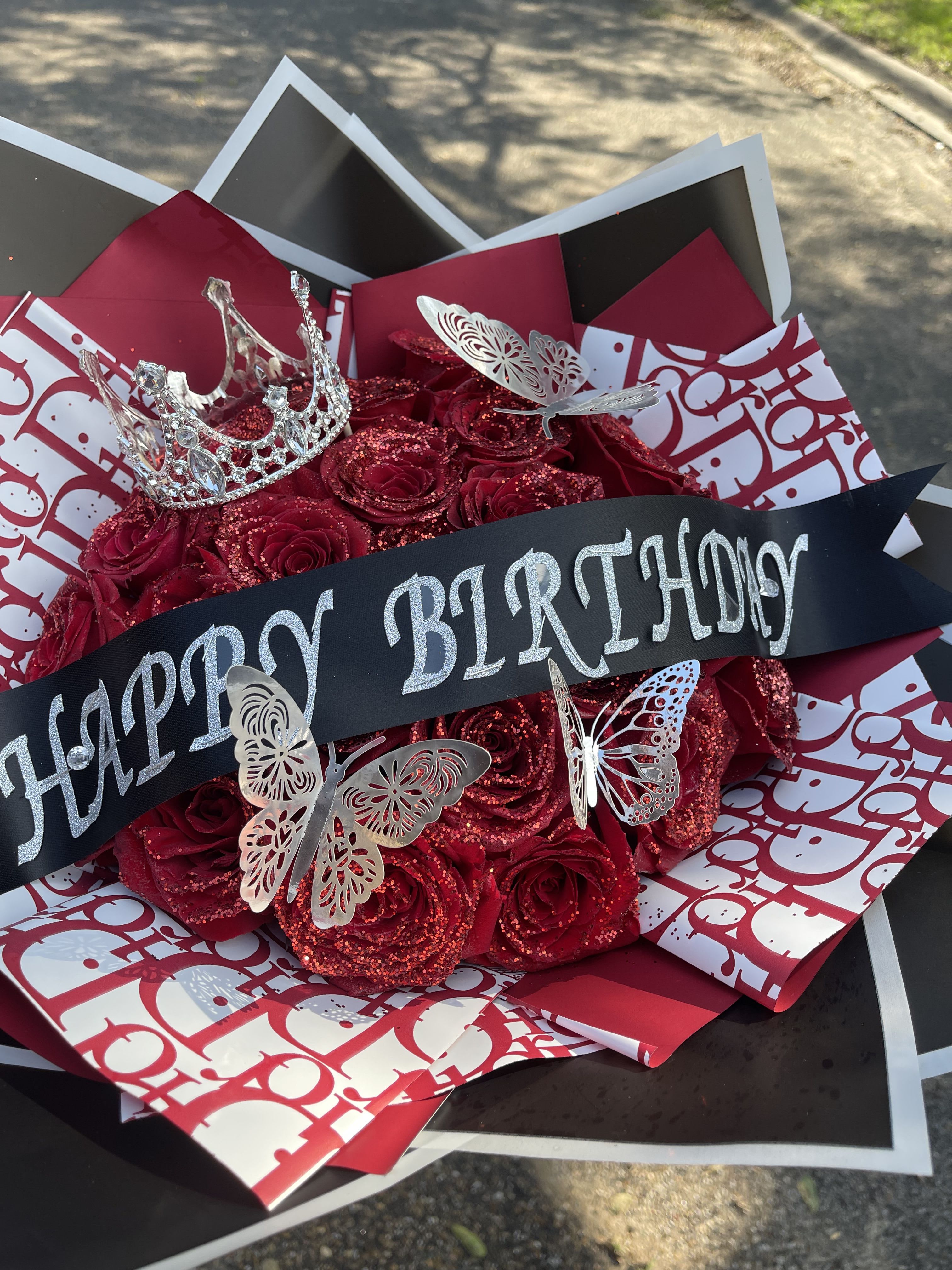 Glitter Rose Bouquet - This arrangement will include  Red Glittered Roses wrapped in paper with a Happy Birthday Banner, Silver butterflies , a crown and black and burgundy Dior paper. * No Vase Included