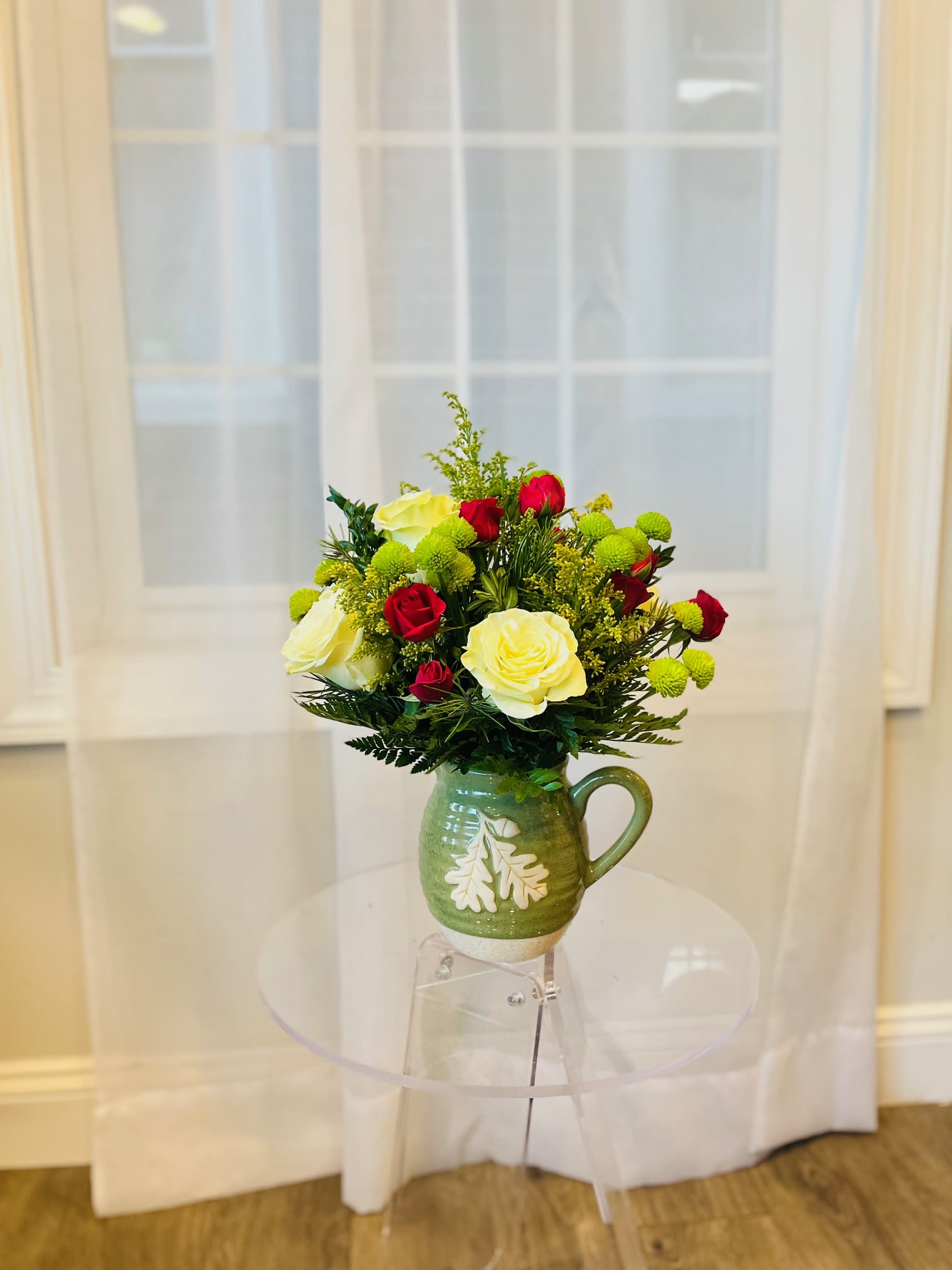 Nana’s Garden *Winter Edition* - Cozy and fresh with a woodsy, holiday feel, this arrangement is designed in a rustic green ceramic keepsake mug featuring a charming leaf detail. It’s filled with a bright mix of creamy white roses, deep red spray roses, and cheerful green button mums, accented with textured seasonal greens and golden filler for a warm, modern winter look. Perfect for gifting—or keeping as a festive touch for your own kitchen, desk, or entryway.